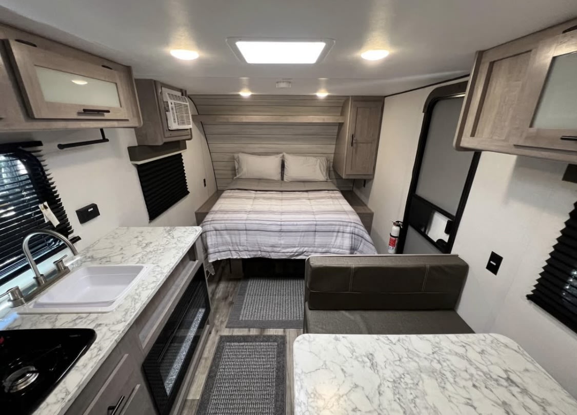 Modern RV rental interior featuring a full bed, compact kitchen with sink/stove, and a dinette for comfy travel.. Dutchmen LT 17R 2024