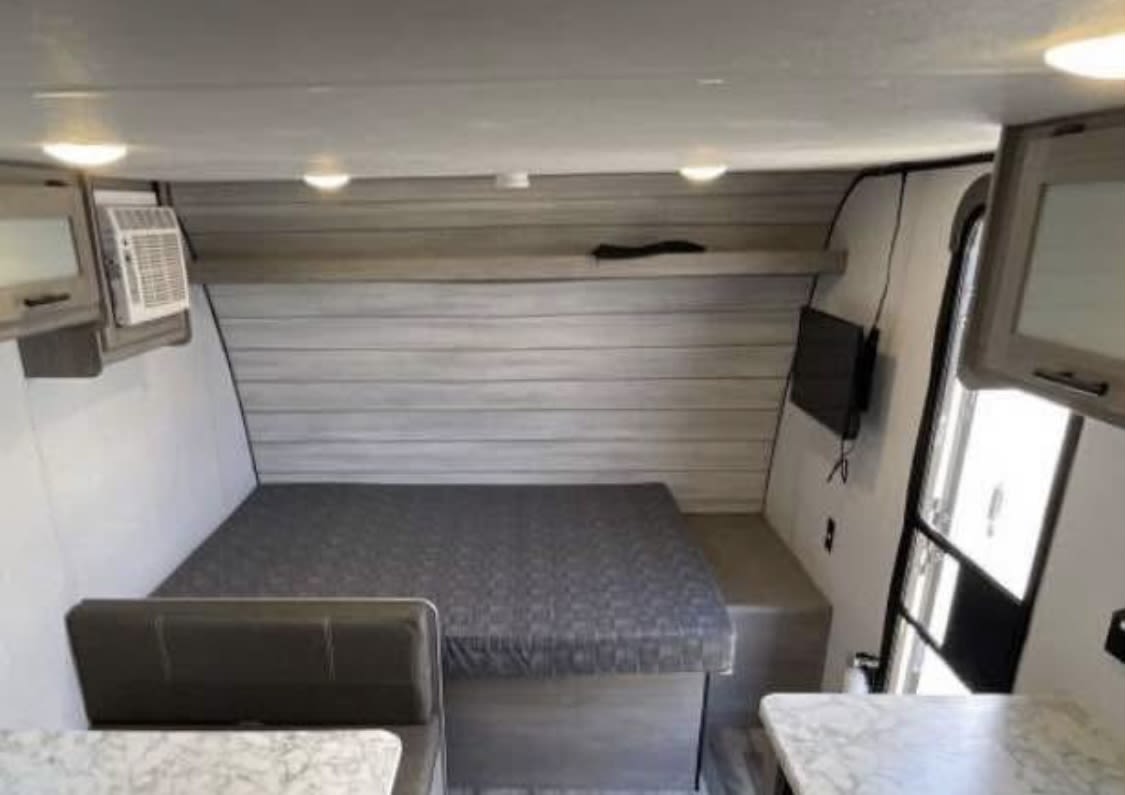 Interior of an RV rental showing a spacious bed/dinette area, mounted TV, and cabinets, ideal for travel.. Dutchmen Other 2024