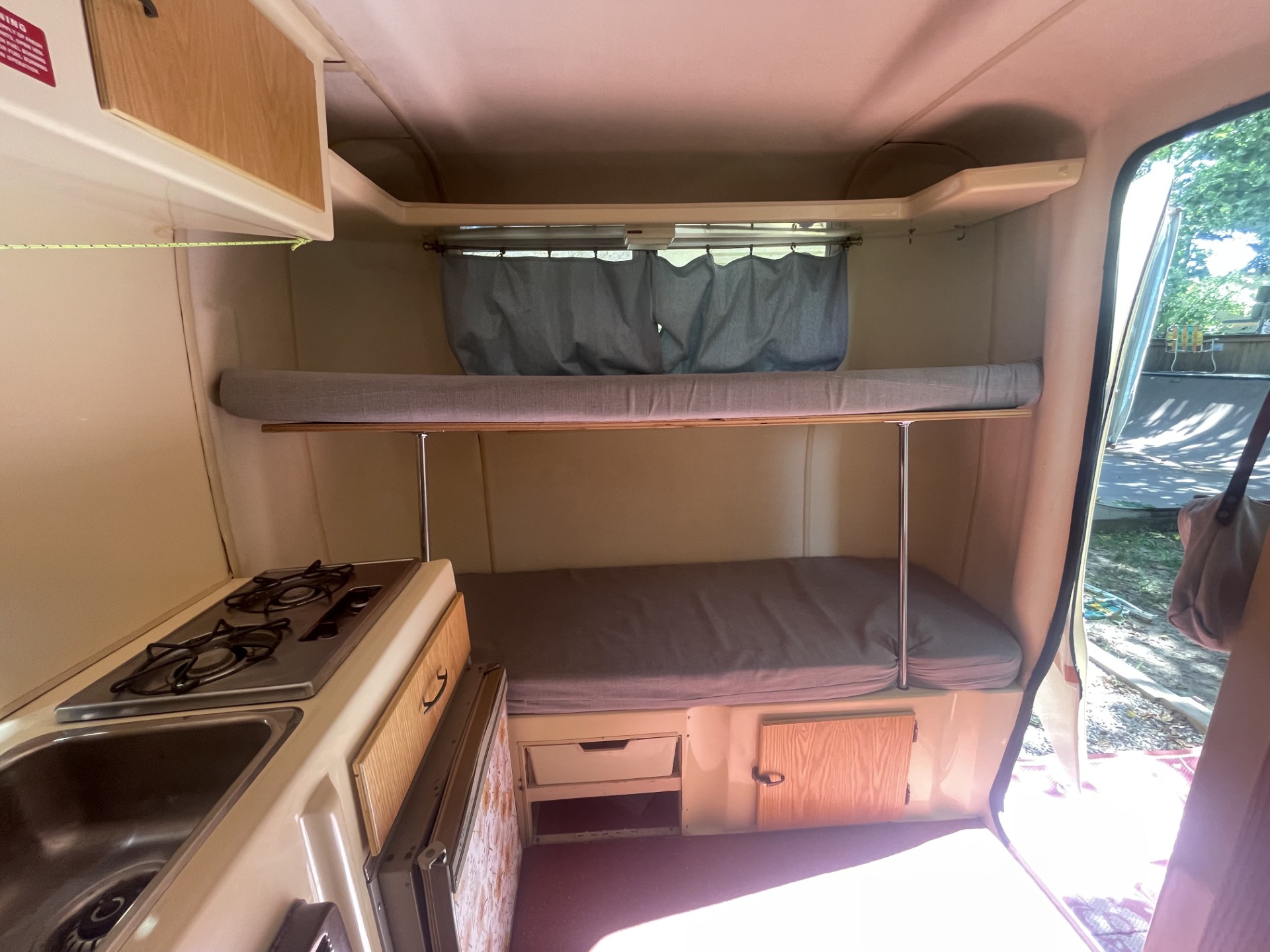 Interior of a compact RV rental showcasing a two-burner kitchen, sink, storage, and cozy bunk beds.. Trillium Rv 130 1976