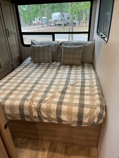Cozy RV rental bedroom with plaid bedding, large window view of the campground, and TV. Perfect for camping trips.. Keystone RV Arcadia 2022
