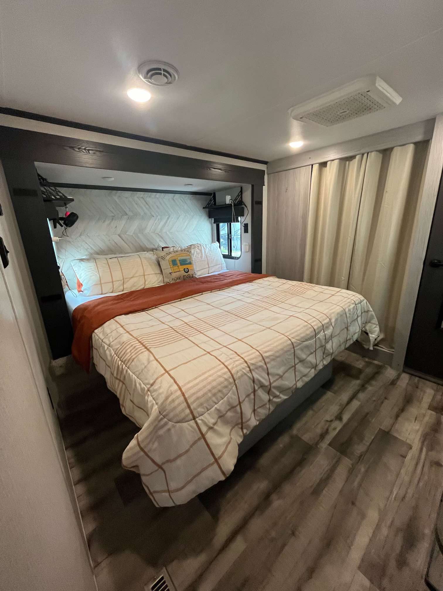 Cozy RV rental bedroom with plaid bedding, chevron headboard, and wood-look flooring. Perfect compact comfort.. Keystone RV Montana 2023