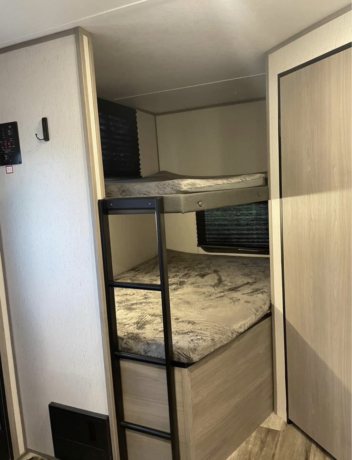 Interior of an RV rental showing two bunk beds with patterned mattresses and a ladder. Ideal for family travel, with utility controls visible.. Dutchmen Coleman Lantern 2022