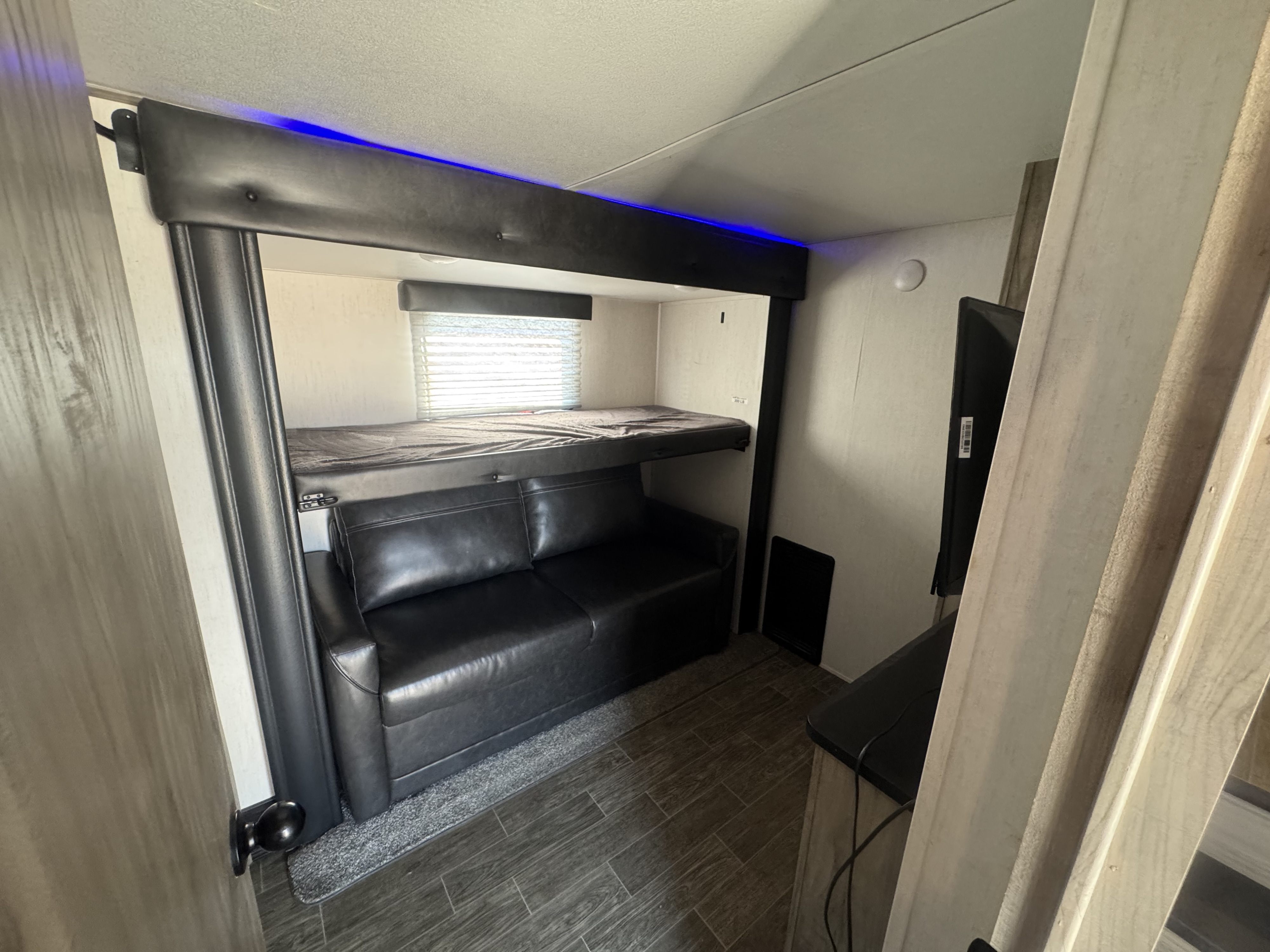 Spacious rv rental interior featuring bunk beds, a convertible sofa, wood-look flooring, and blue LED accent lighting.. Forest River Cherokee Arctic Wolf 2022