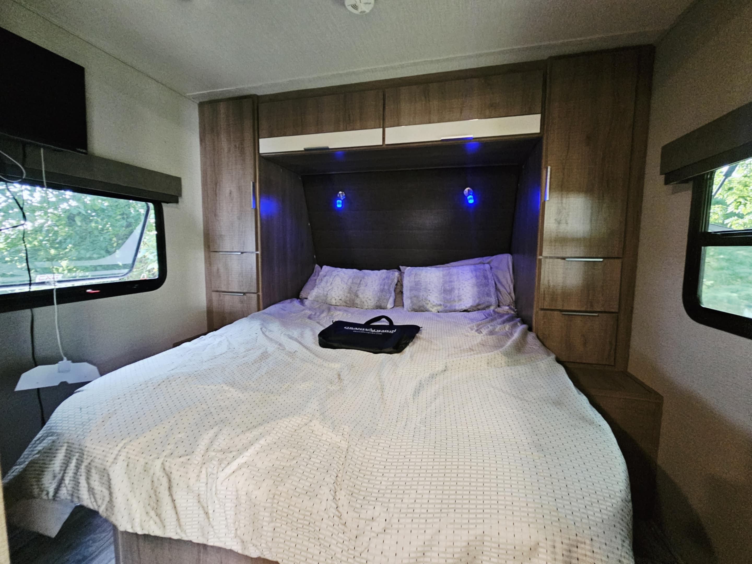 Cozy RV rental bedroom featuring a comfortable bed, overhead storage, TV, and ambient blue lighting for your travels.. Grand Design Imagine XLS 2020