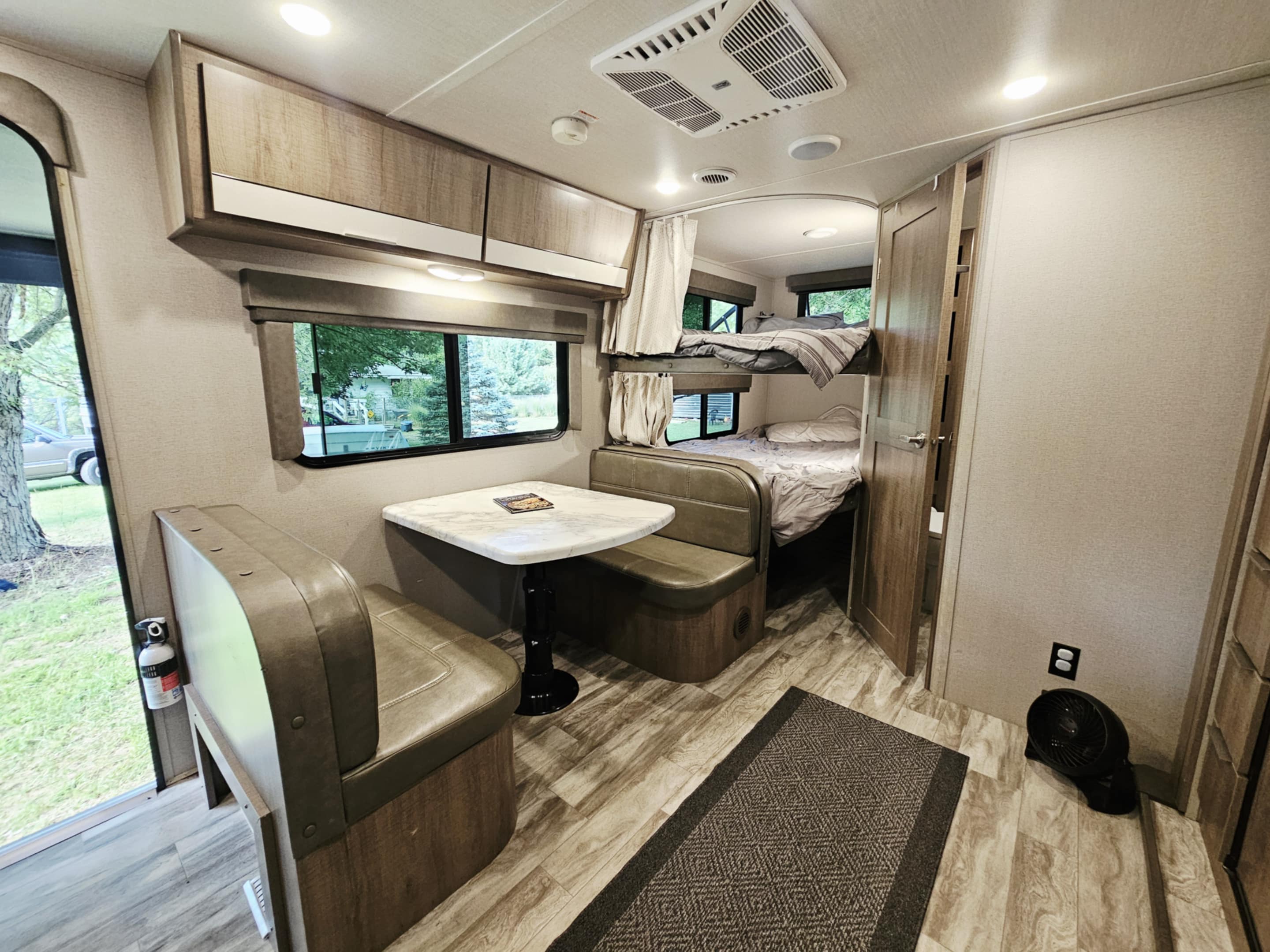 Bright rv rental interior showing a dining area, overhead cabinets, and bunk beds in a cozy travel trailer.. Grand Design Imagine XLS 2020