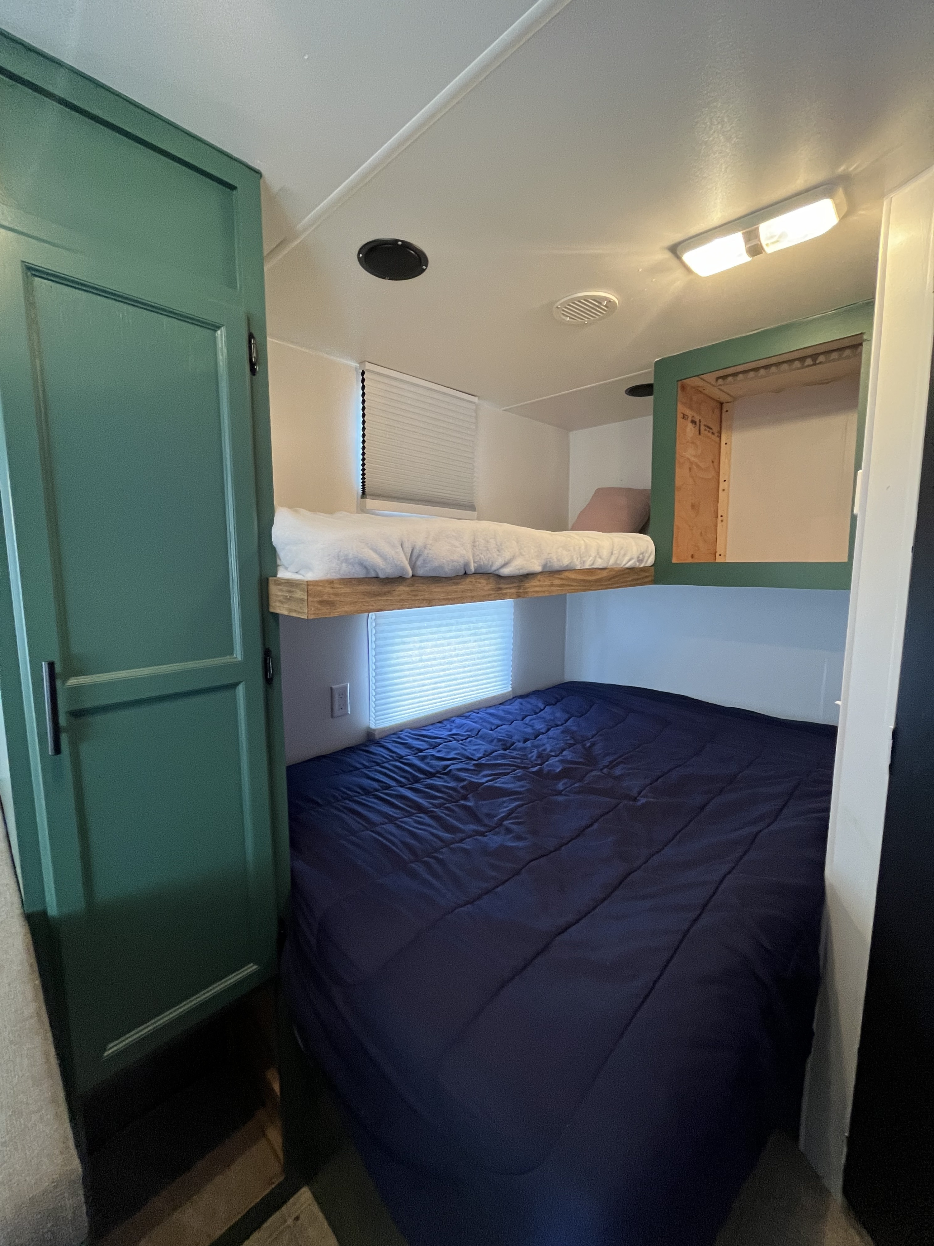 Cozy sleeping space in an RV rental featuring bunk beds. The lower bed has blue bedding, upper has white, with green cabinetry.. Pioneer TT 2007