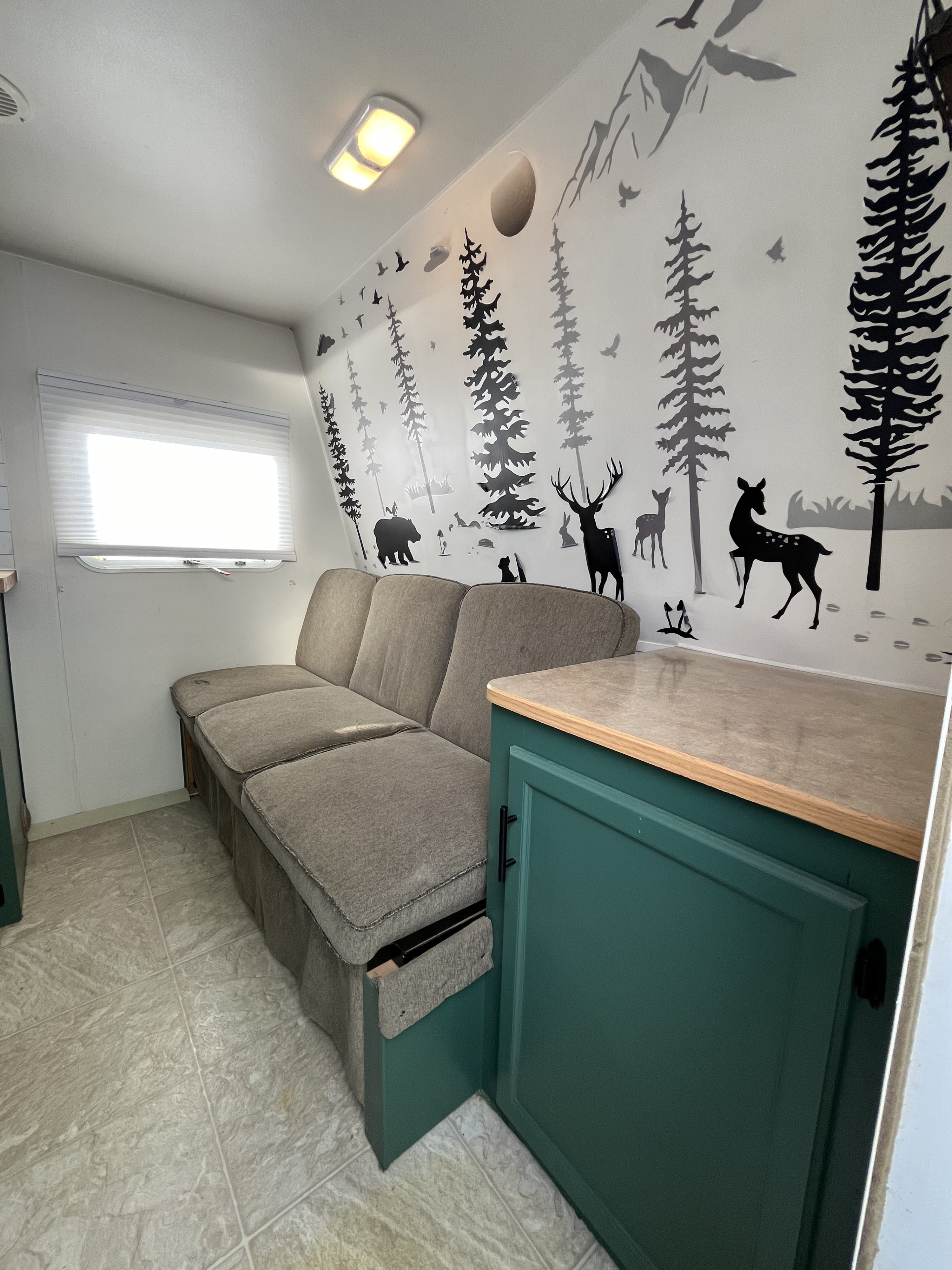 Cozy RV rental interior with a long sofa, nature-themed wall decals (trees, animals), and practical green storage.. Pioneer TT 2007