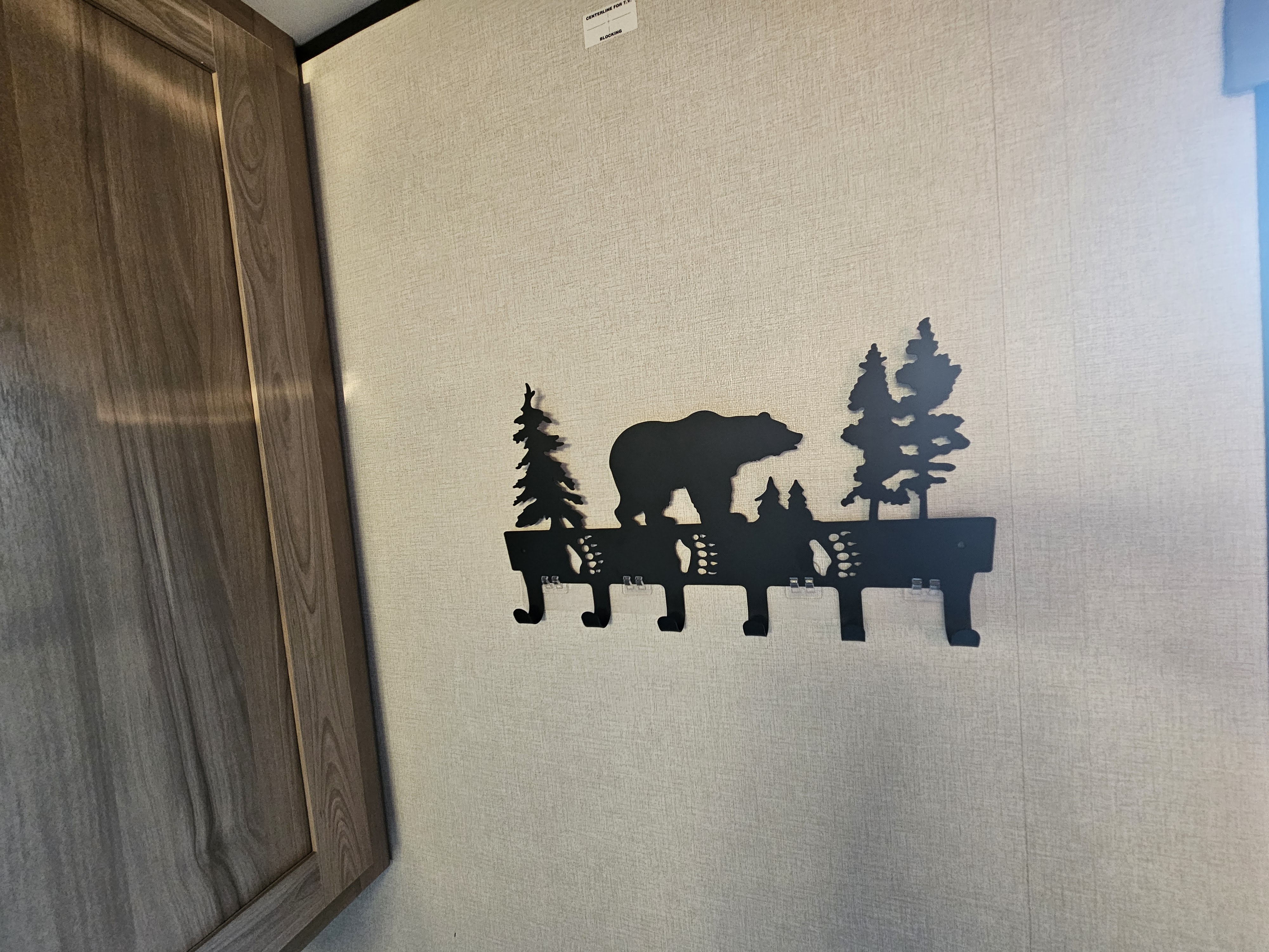 Black metal bear and tree coat rack with 5 hooks on an RV wall, next to a wooden cabinet. Perfect for an rv rental.. Coleman 17b 2025