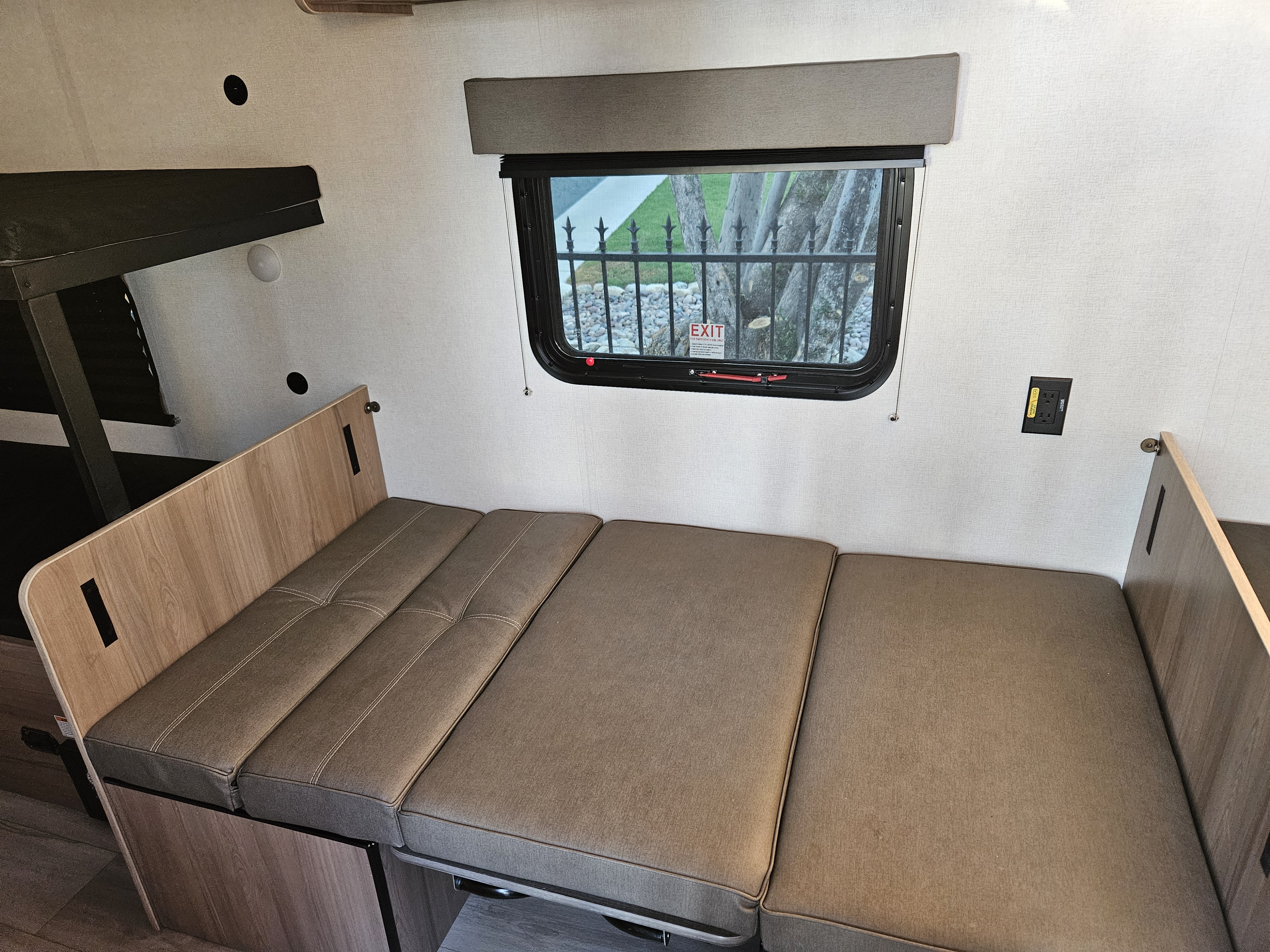 Bright RV rental interior with a brown convertible bench seat/bed, overhead bunk, and an emergency exit window.. Coleman 17b 2025