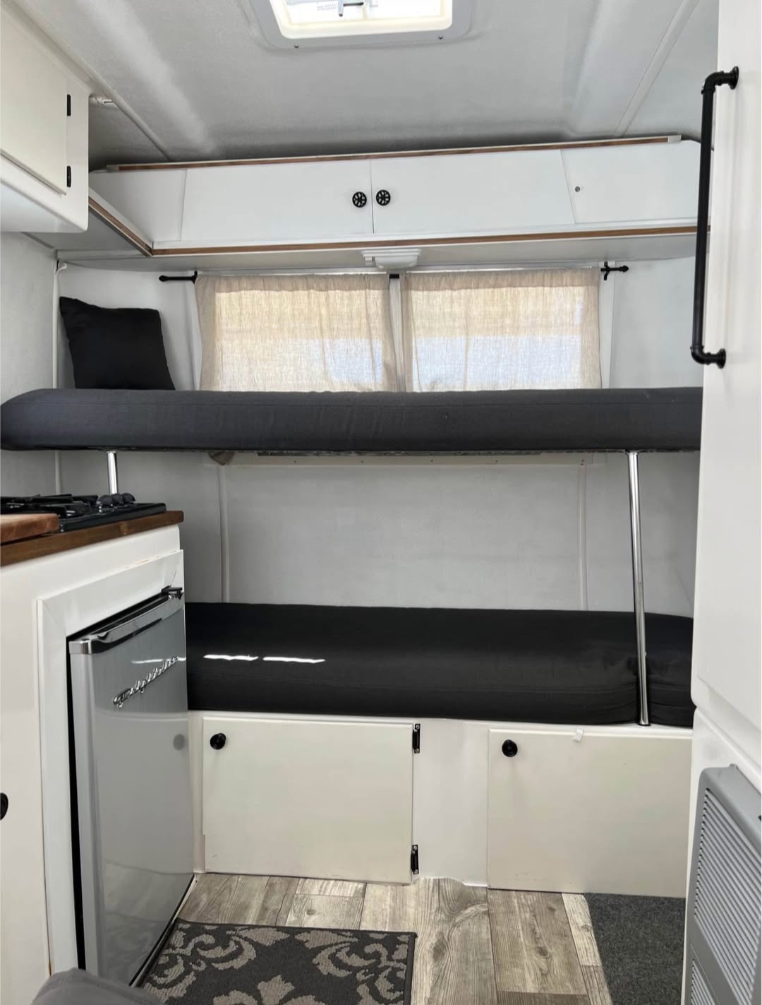 Inside an RV rental: white interior with black bunk beds, compact fridge, overhead cabinets, and wood-look floor. Cozy camper space.. Trillium Rv Trillium 4500 1977