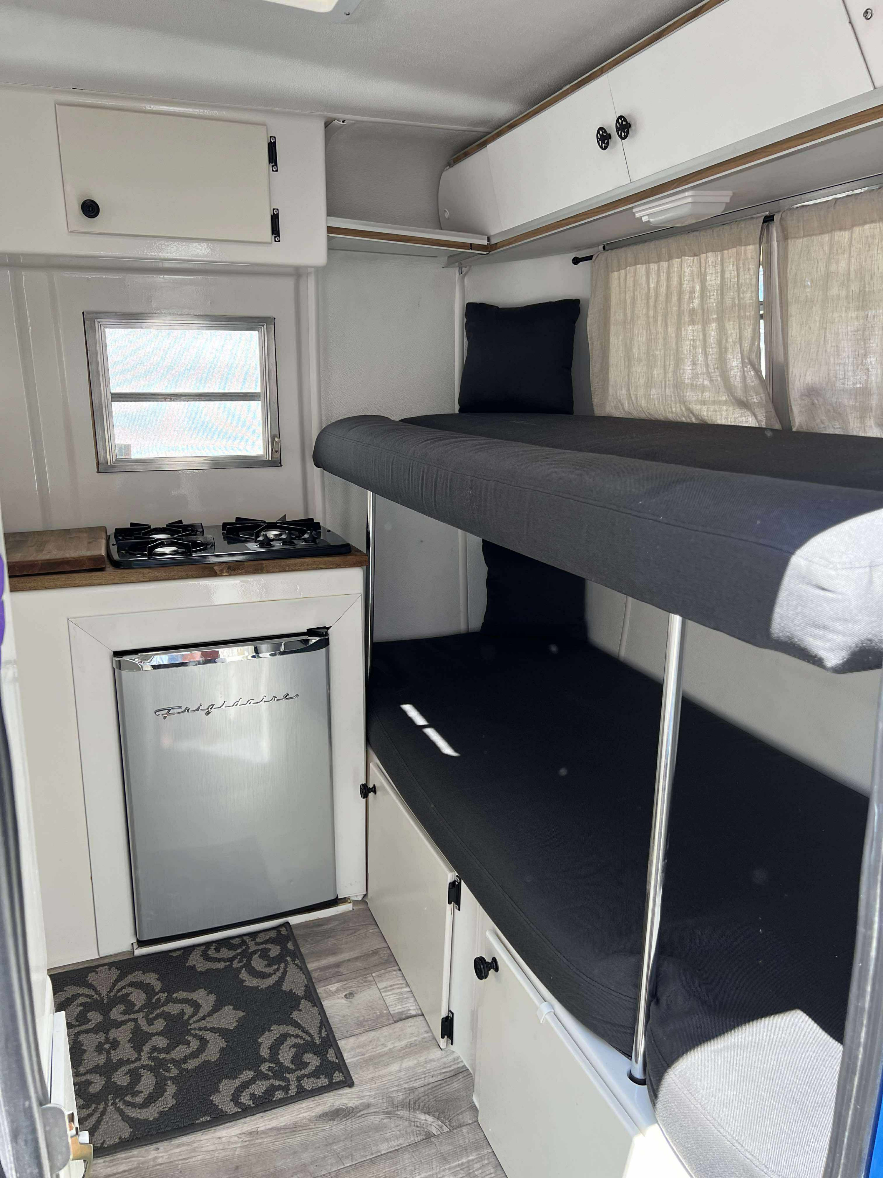 Cozy RV rental interior with a compact kitchen (stove, Frigidaire fridge, counter), bunk beds, and overhead cabinets.. Trillium Rv Trillium 4500 1977