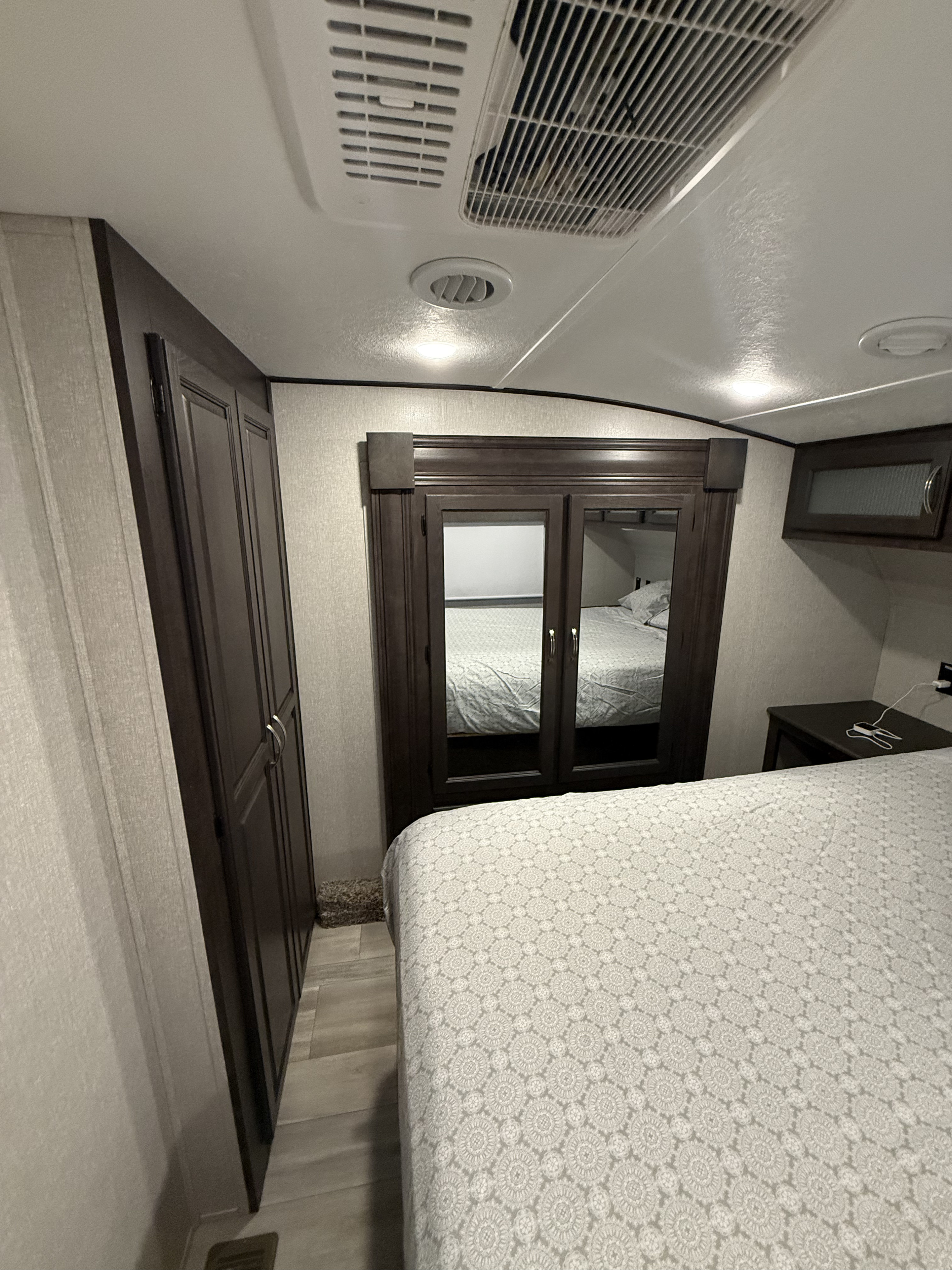 Cozy RV rental bedroom with a comfy patterned bed, mirrored wardrobe, ample storage, and ceiling AC unit for pleasant travels.. Shasta Phoenix 367BH 2022