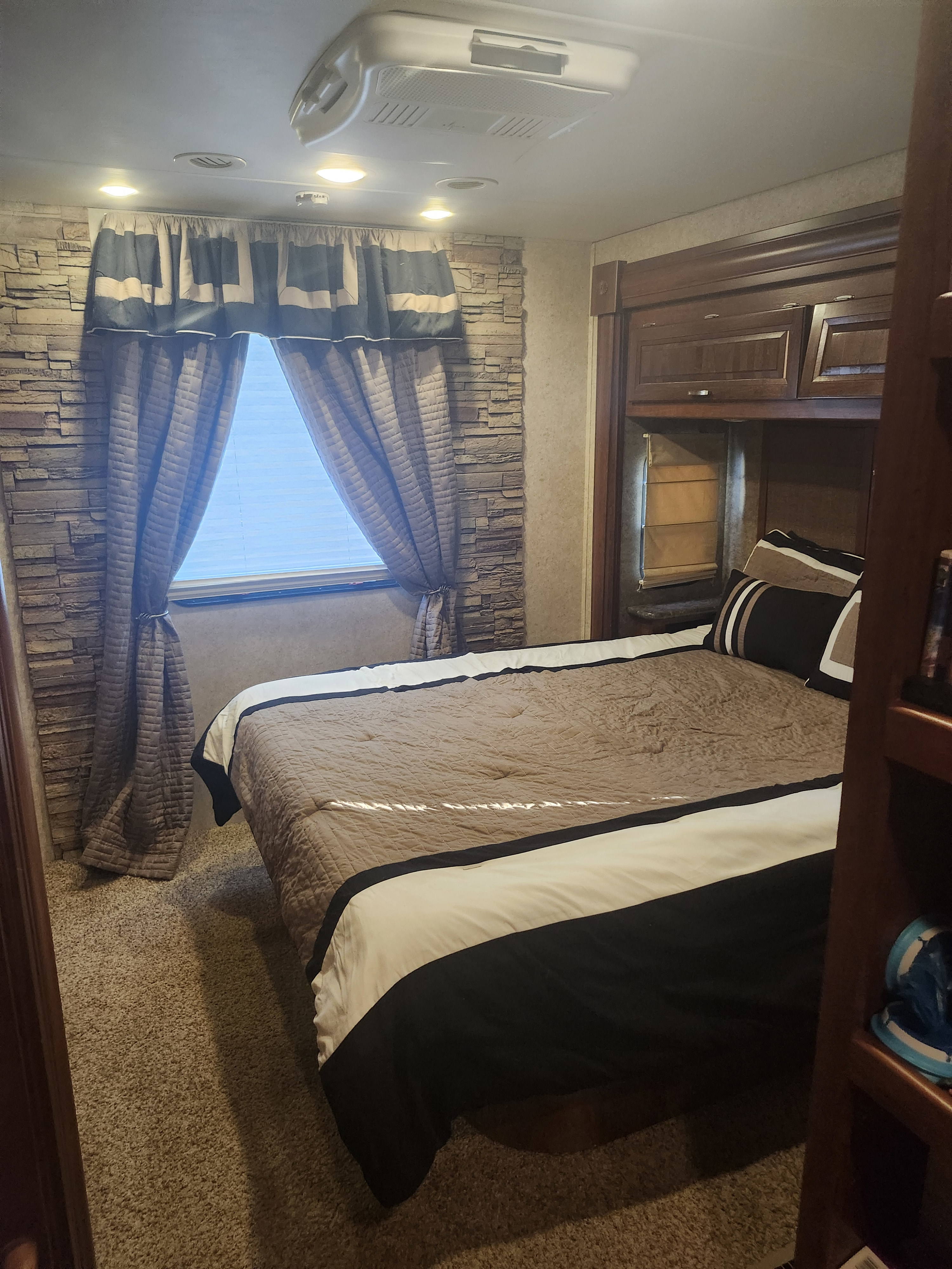 Cozy RV rental bedroom: brown and white bed, decorative curtains, stone accent wall, and wood cabinetry.. Forest River Georgetown ts351 2013