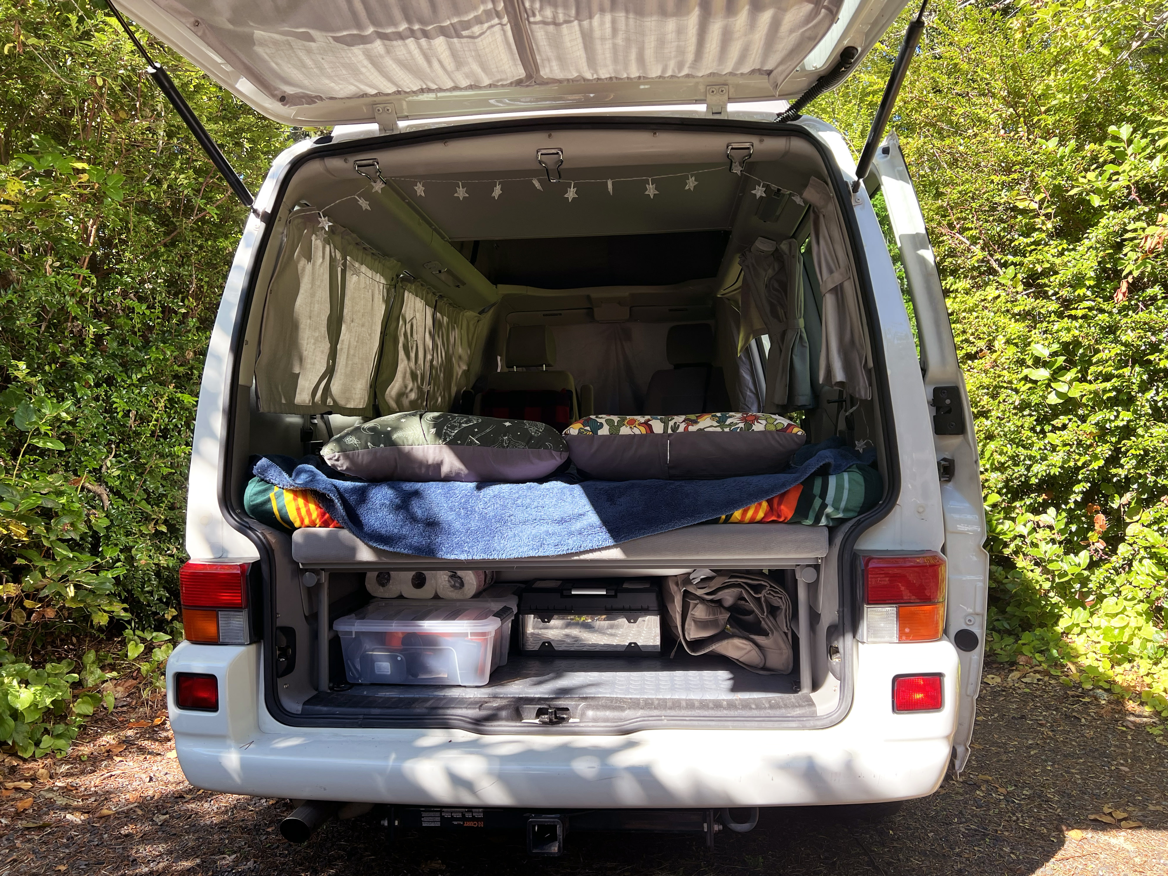 Open rear hatch of an RV rental, showing the cozy bed and organized storage inside for camping adventures.. Volkswagen T4 Multivan Westfalia 2003