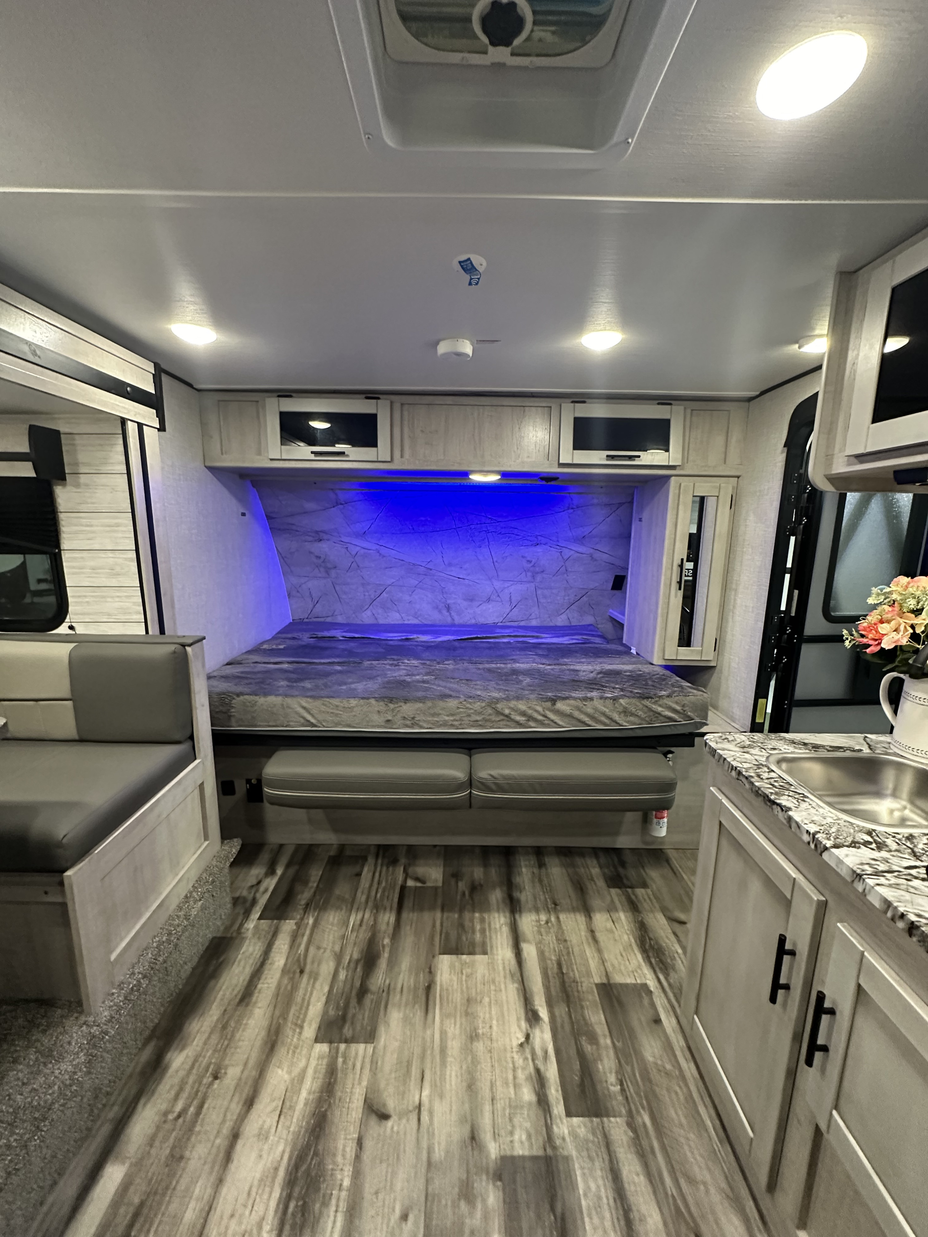 Spacious RV rental interior with a bed featuring ambient blue lighting, a convertible dinette, and a functional kitchenette.. Crossroads RV Sunset Trail 2023