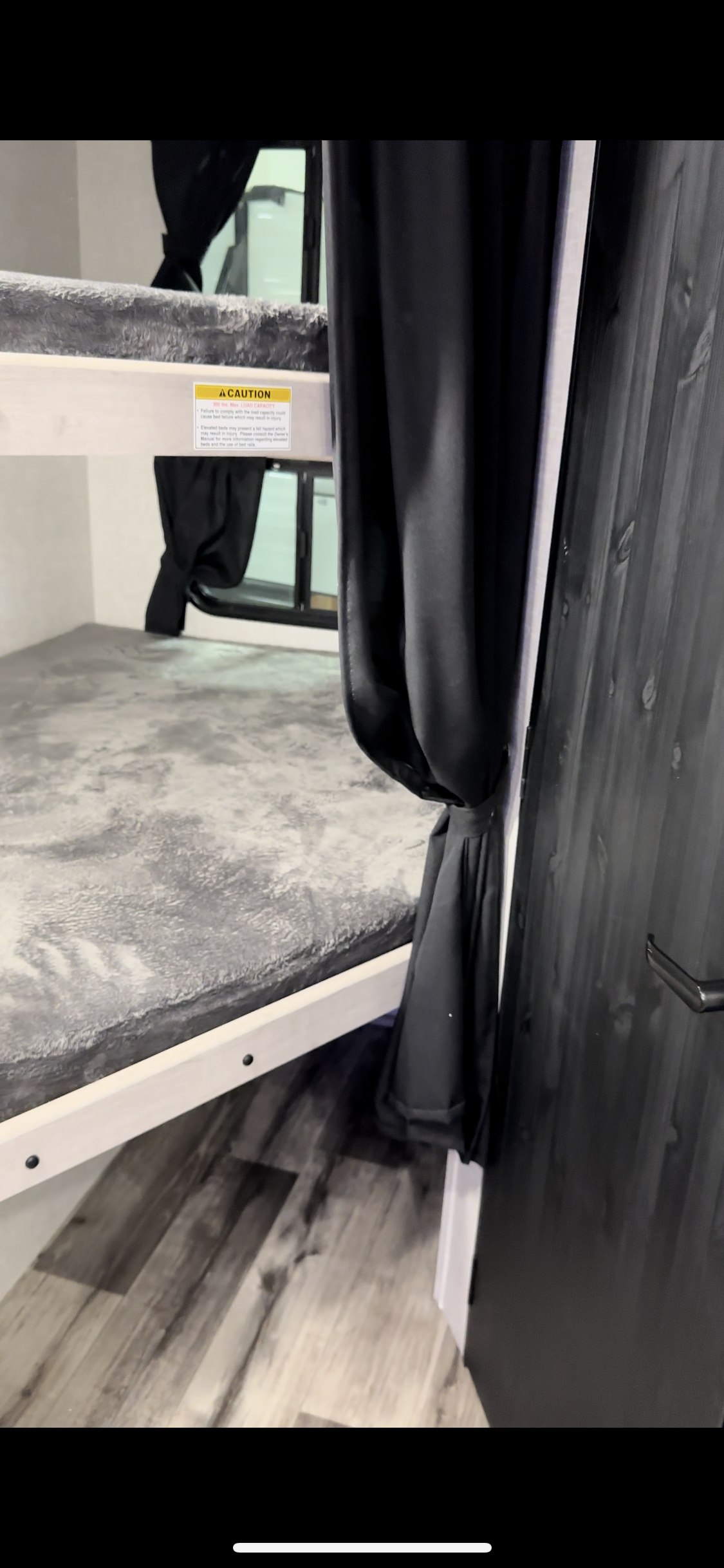 Bunk beds in an RV rental, featuring soft grey bedding, black privacy curtains, and a safety warning label on the top bunk.. Crossroads RV Sunset Trail 2023