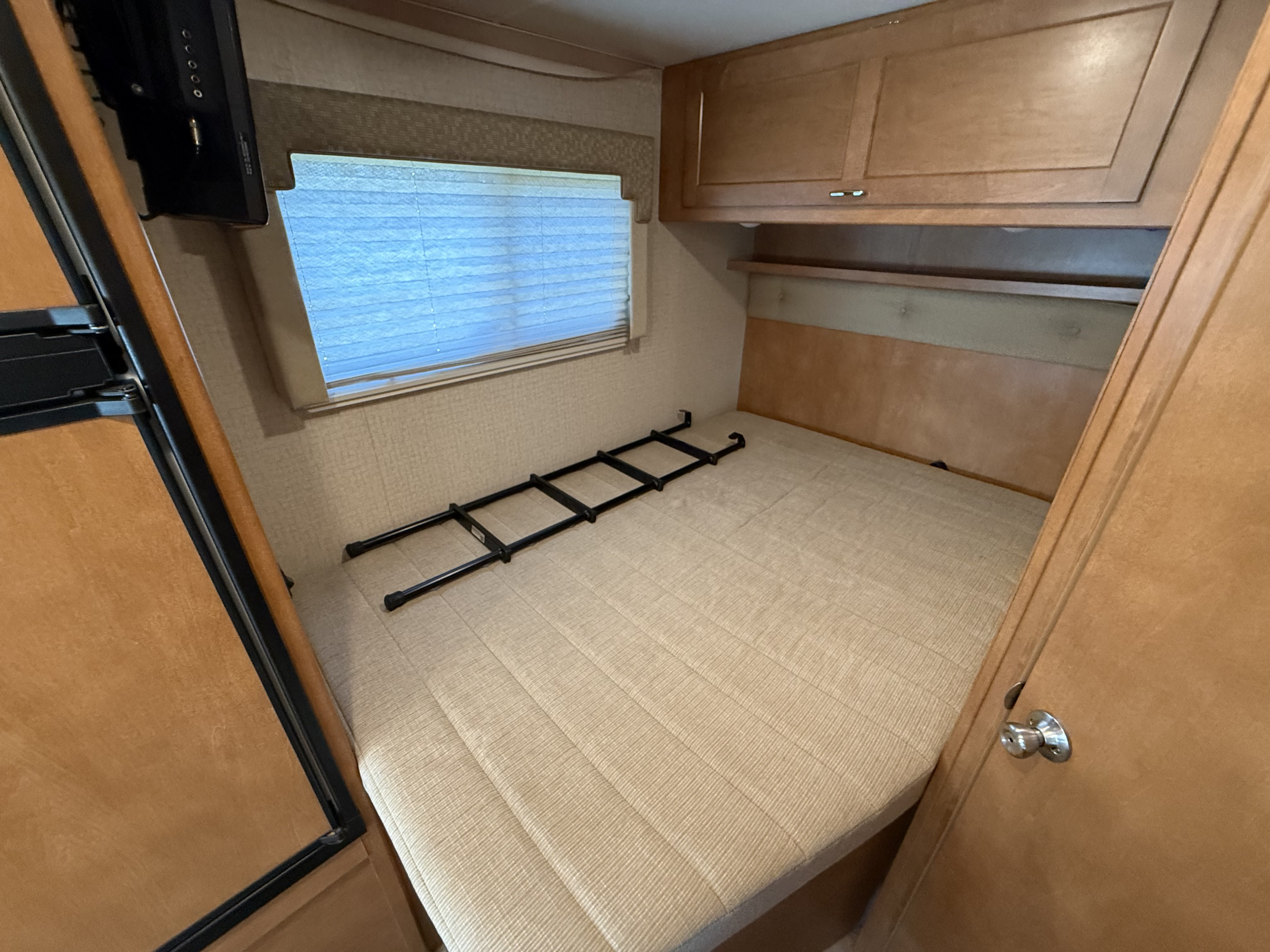 RV rental bedroom interior featuring a bed, window, TV, and wood cabinets. A ladder is on the bed.. Winnebago Minnie Winnie 2017