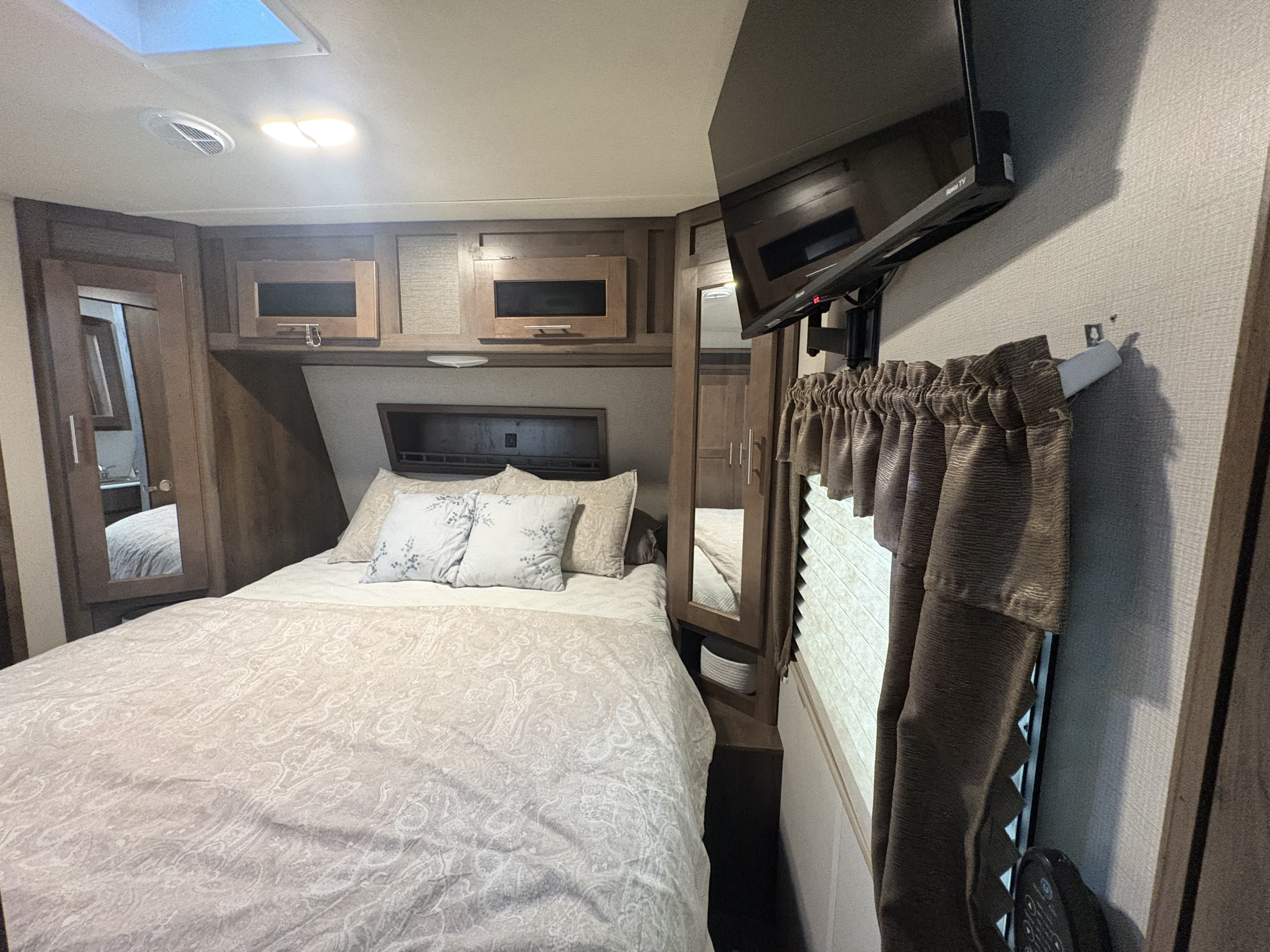 Cozy RV rental bedroom featuring a comfortable bed with patterned bedding, overhead storage, and a mounted TV.. Forest River Wildcat 2019