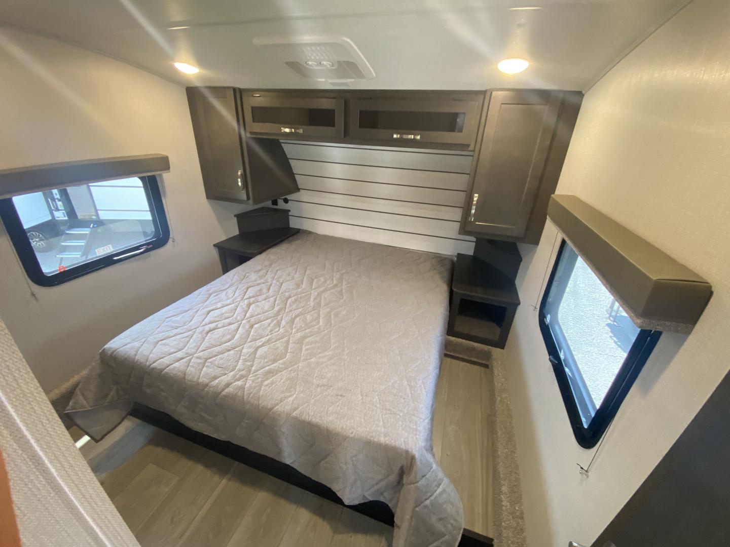 Cozy RV rental bedroom featuring a comfy bed, overhead cabinets, and dual windows, ideal for compact living.. Keystone RV Cougar 2024