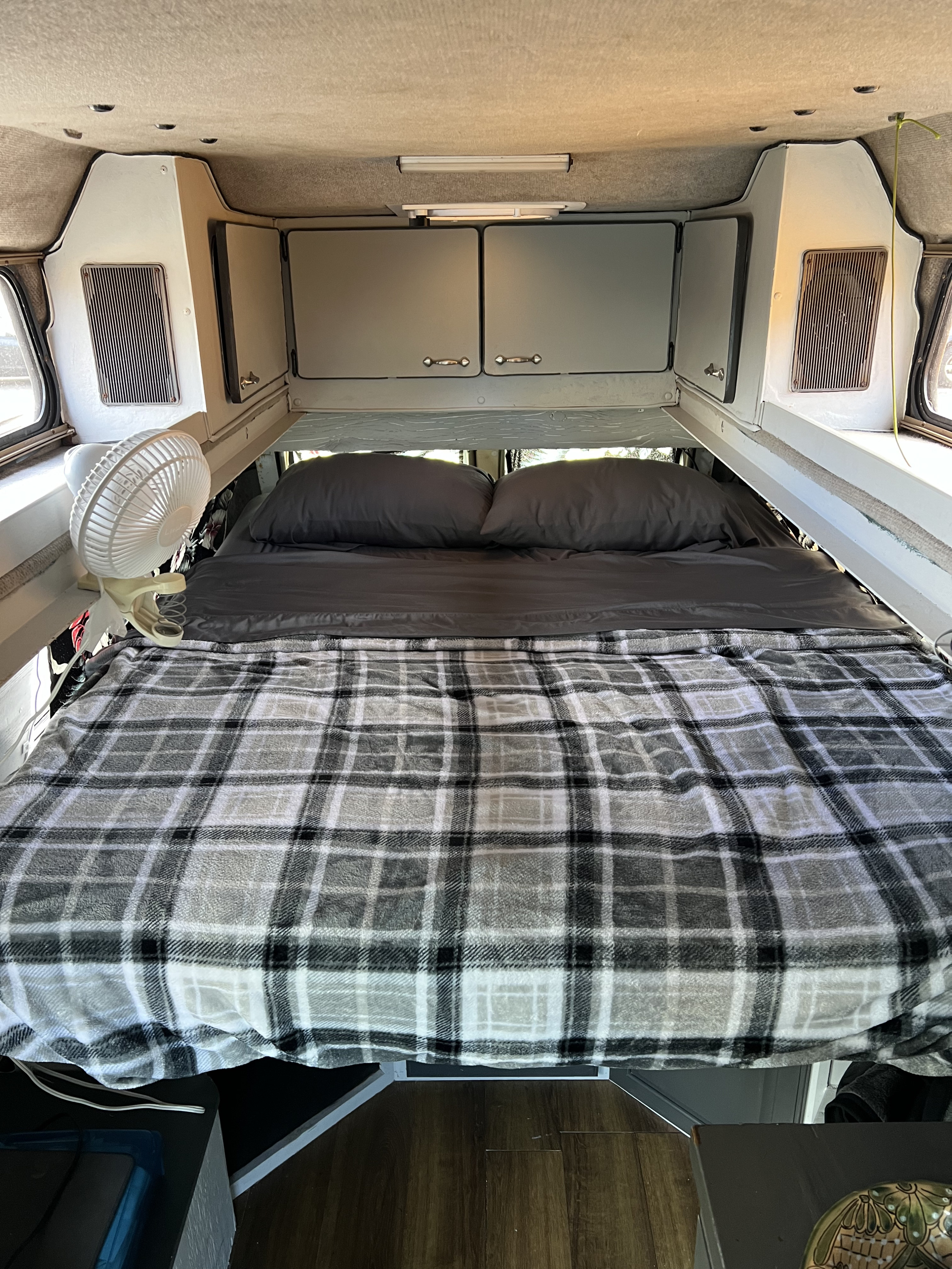Cozy RV rental sleeping area with comfy bed, overhead cabinets, and a clip-on fan for comfort.. Dodge B Van 1994