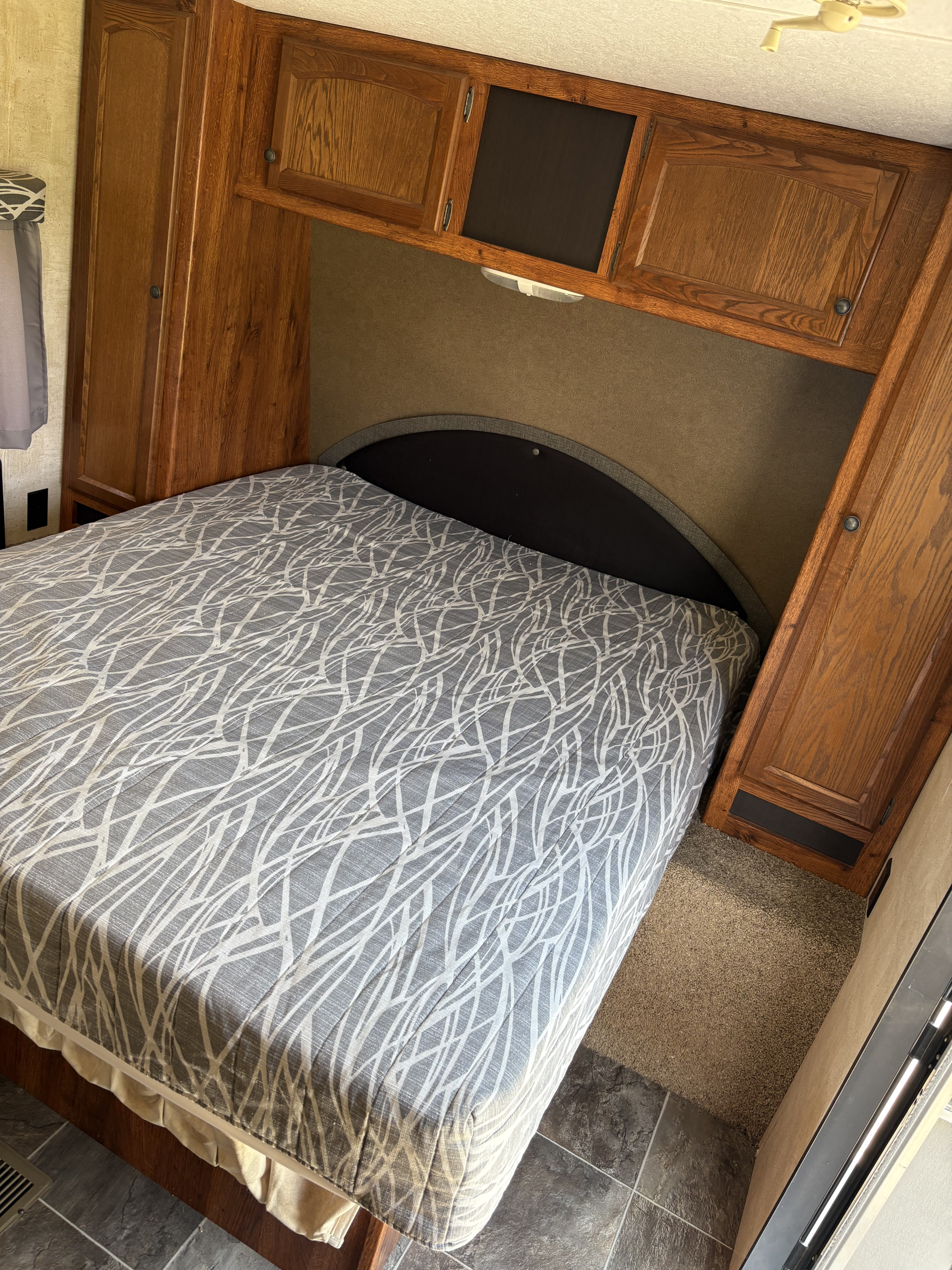 Inside an RV rental: a compact bedroom with a patterned bed, built-in wooden cabinets, and a cozy headboard.. Keystone RV Hideout 2015