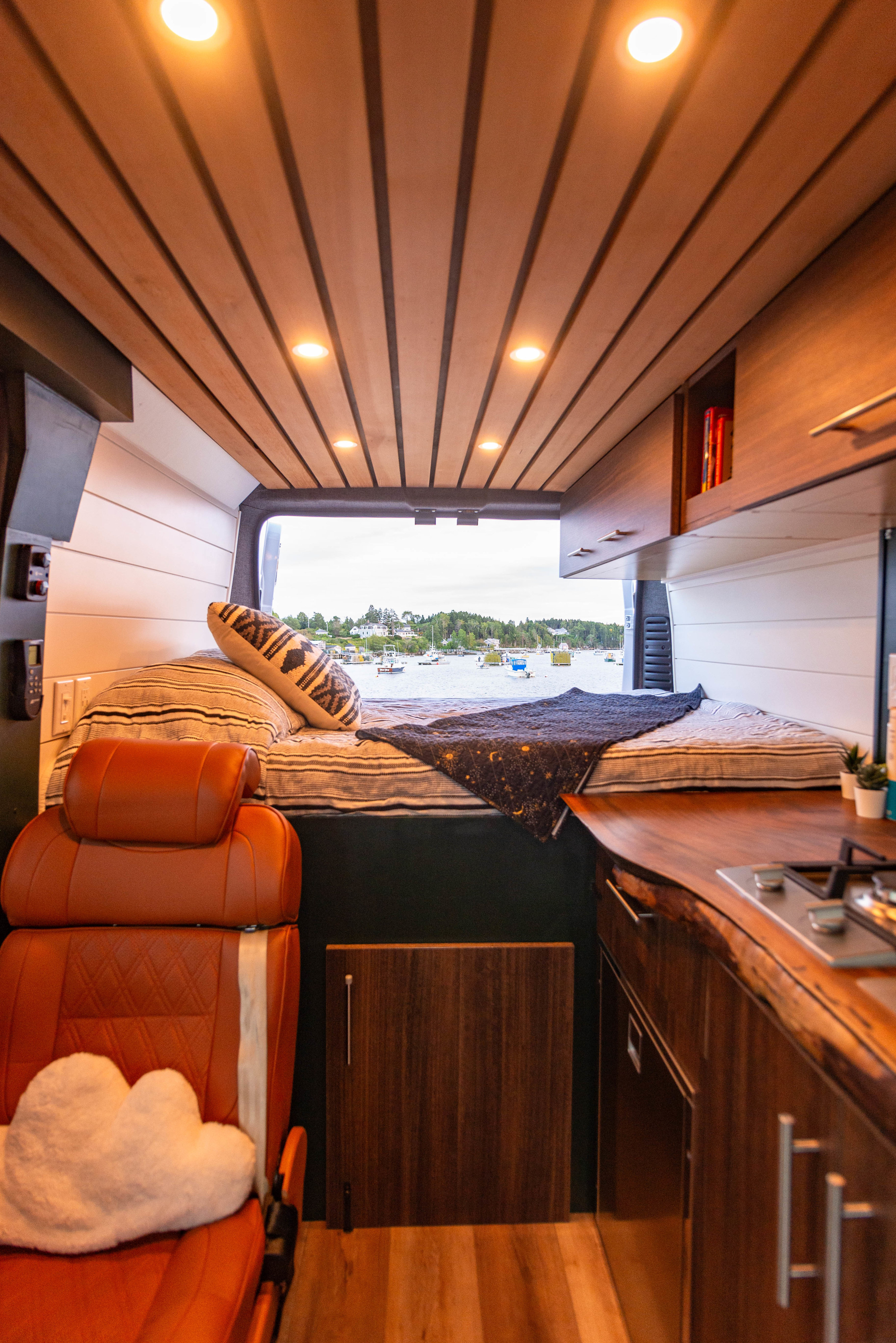 Inside this custom RV rental: wood-paneled ceiling, comfy bed, and a kitchen area, all with an ocean view.. Dodge Ram Promaster 2500 2020