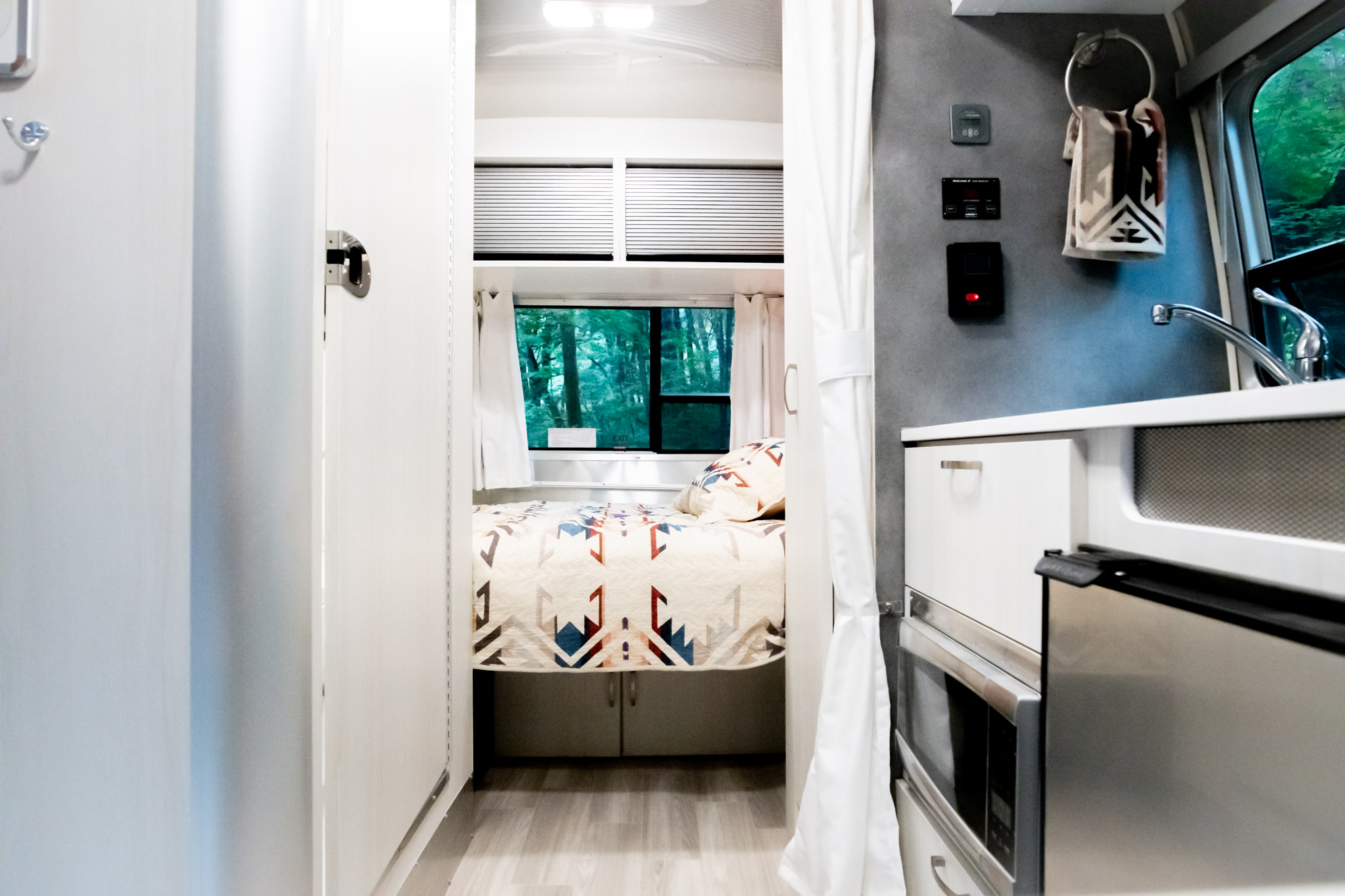 Bright, cozy rv rental interior. Comfortable bed with forest views, plus a compact kitchen. Ideal for your next road trip.. Airstream Bambi 2022