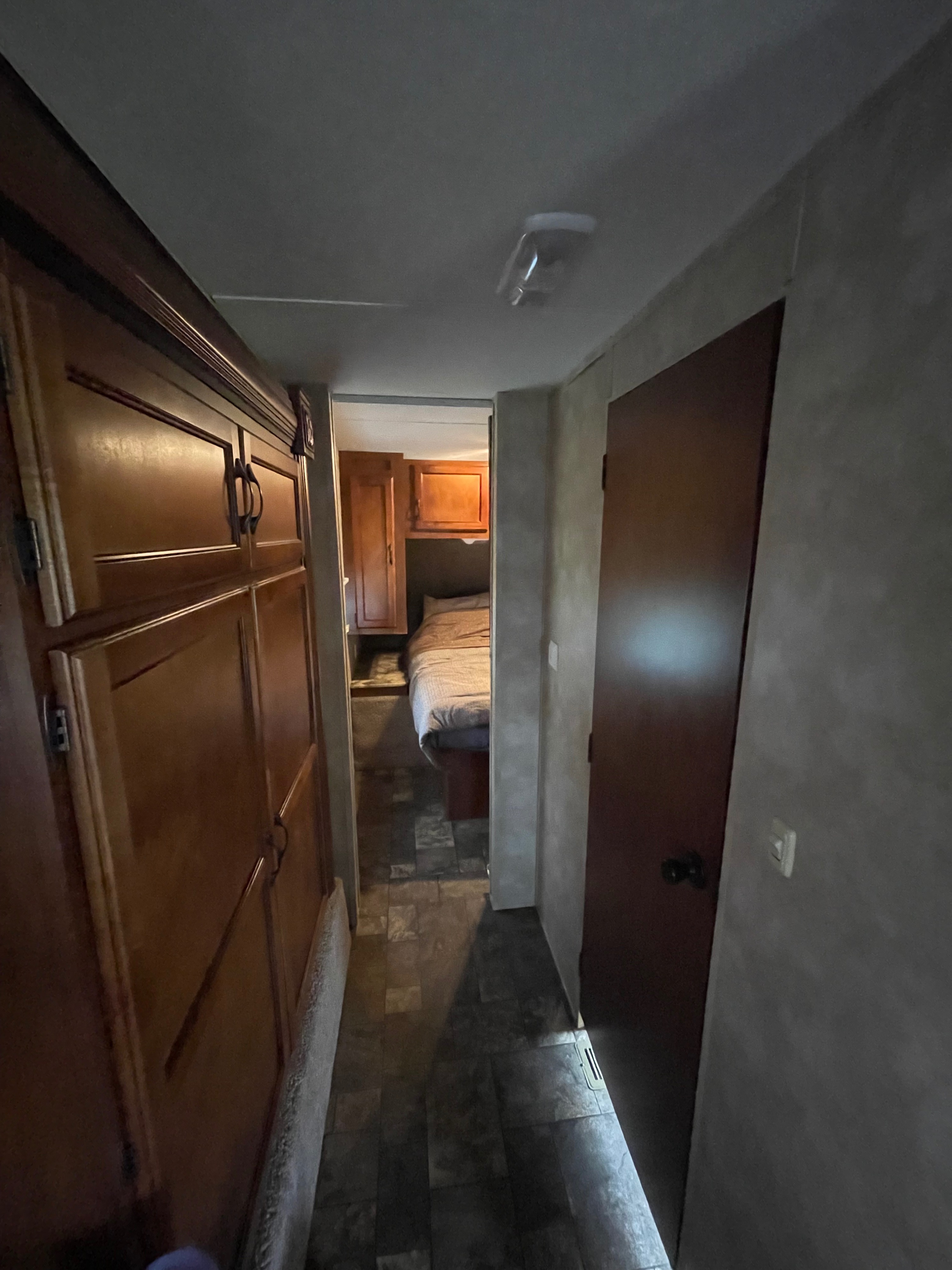An RV rental interior shows a narrow hallway with dark wood cabinetry on the left, leading to a bed in a small bedroom.. Coachmen Catalina Deluxe Edition 2013