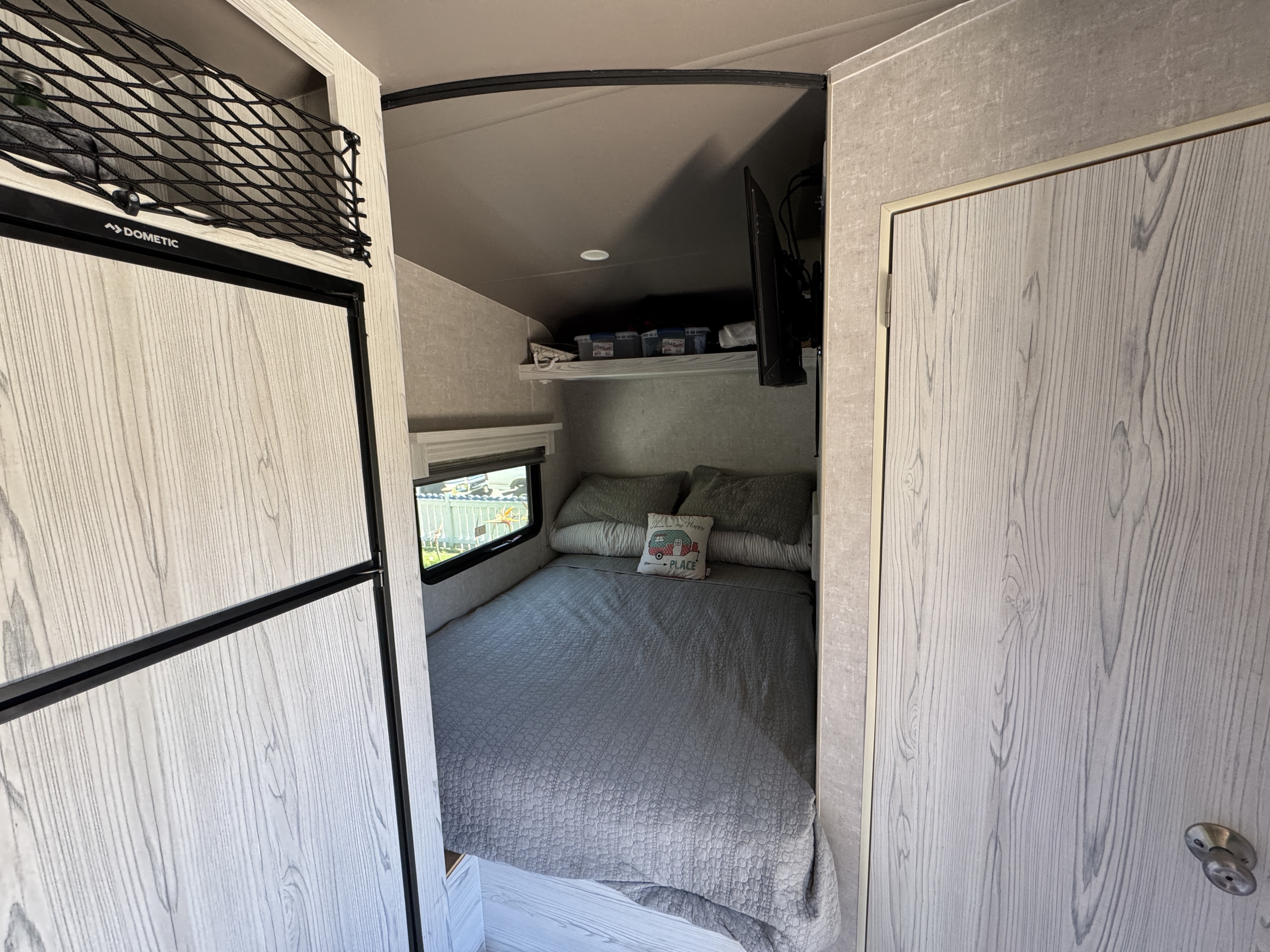 Cozy rv rental interior: bedroom with bed, Dometic fridge, overhead net storage, wall-mounted TV, and light wood grain.. Eclipse Recreational Vehicles Iconic 2022