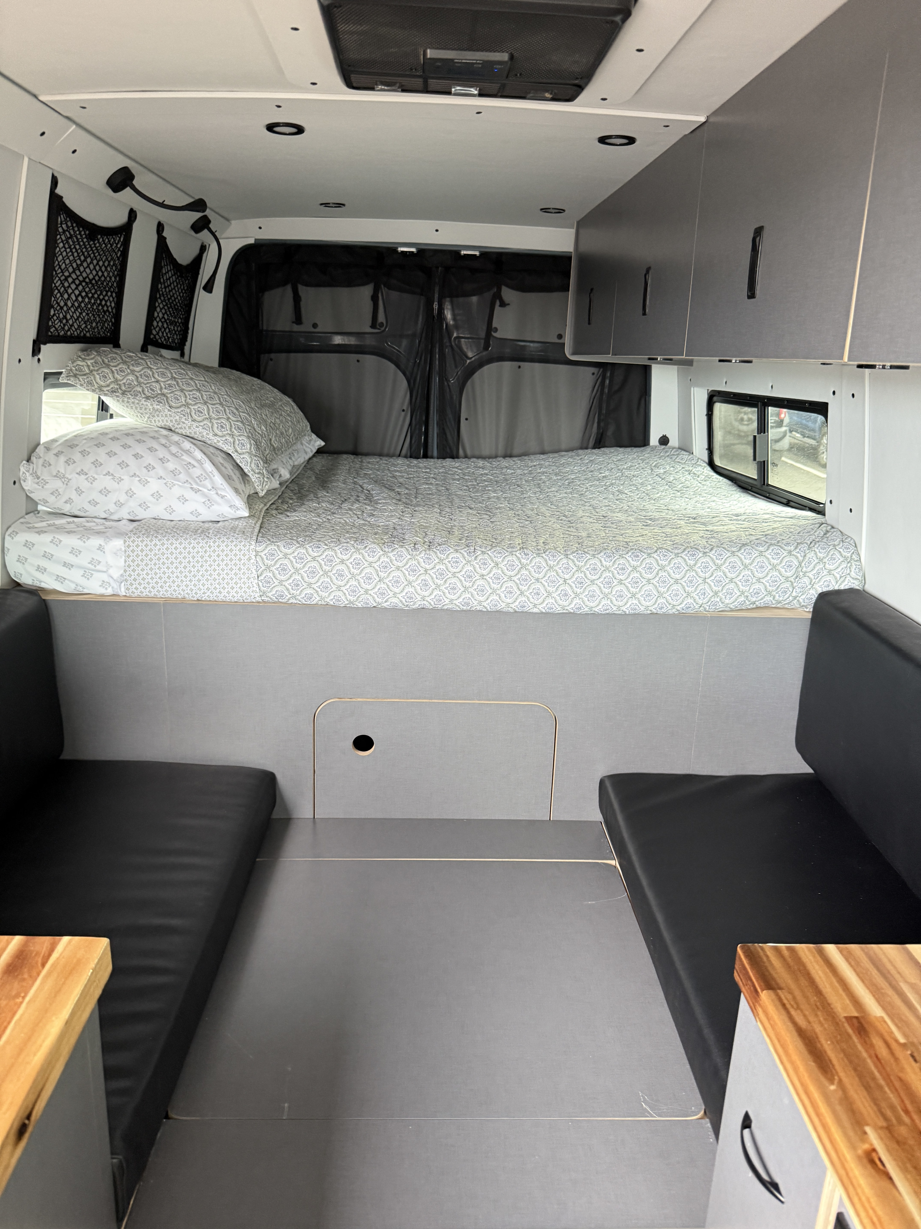 Inside a cozy rv rental: queen bed with patterned bedding, dual seating areas, and sleek overhead cabinets.. Mercedes Sprinter 2024