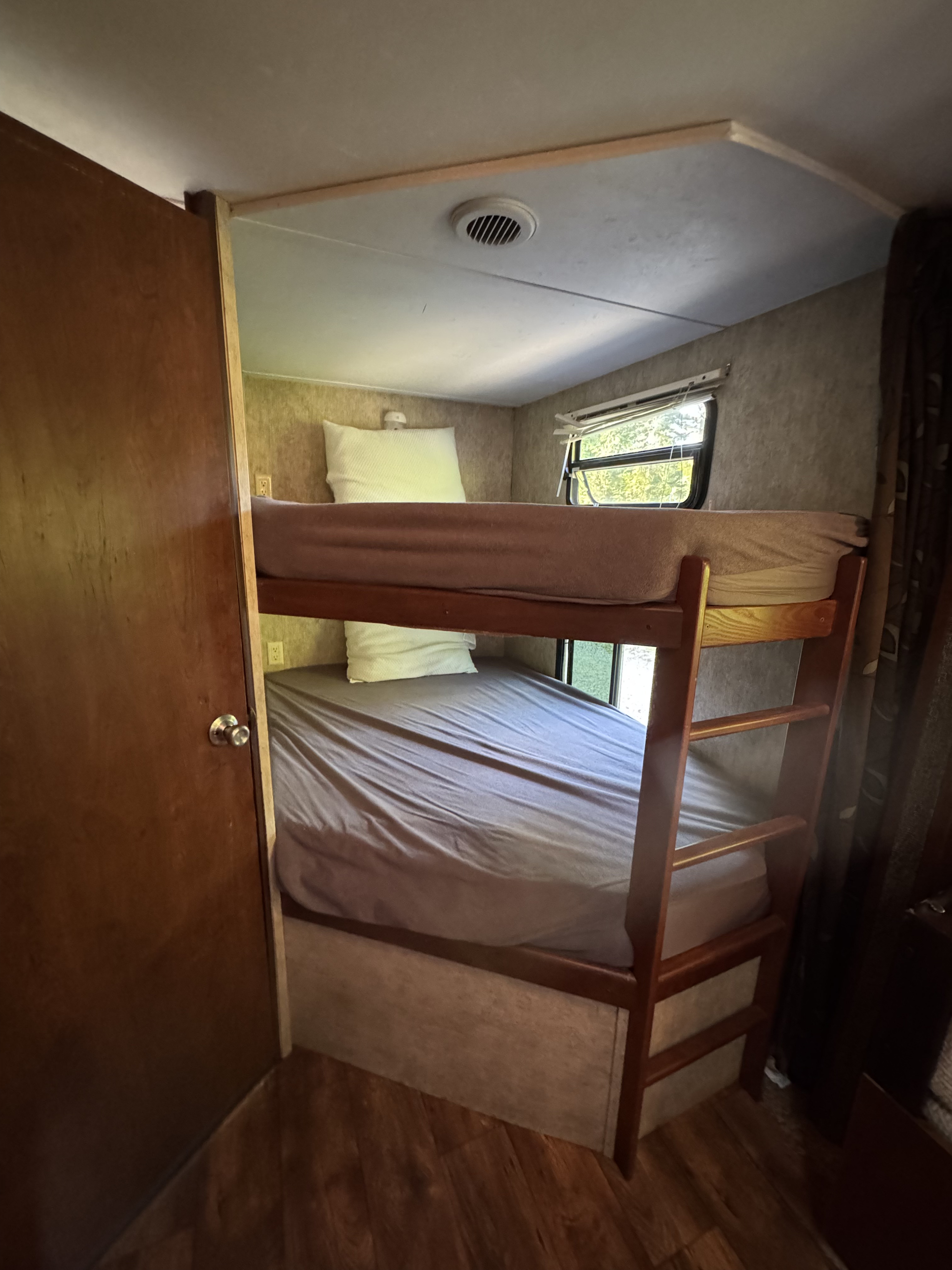 RV rental with compact bunk beds, featuring a top and bottom bunk, window, and wood-look flooring.. Keystone RV Passport Grand Touring 2016