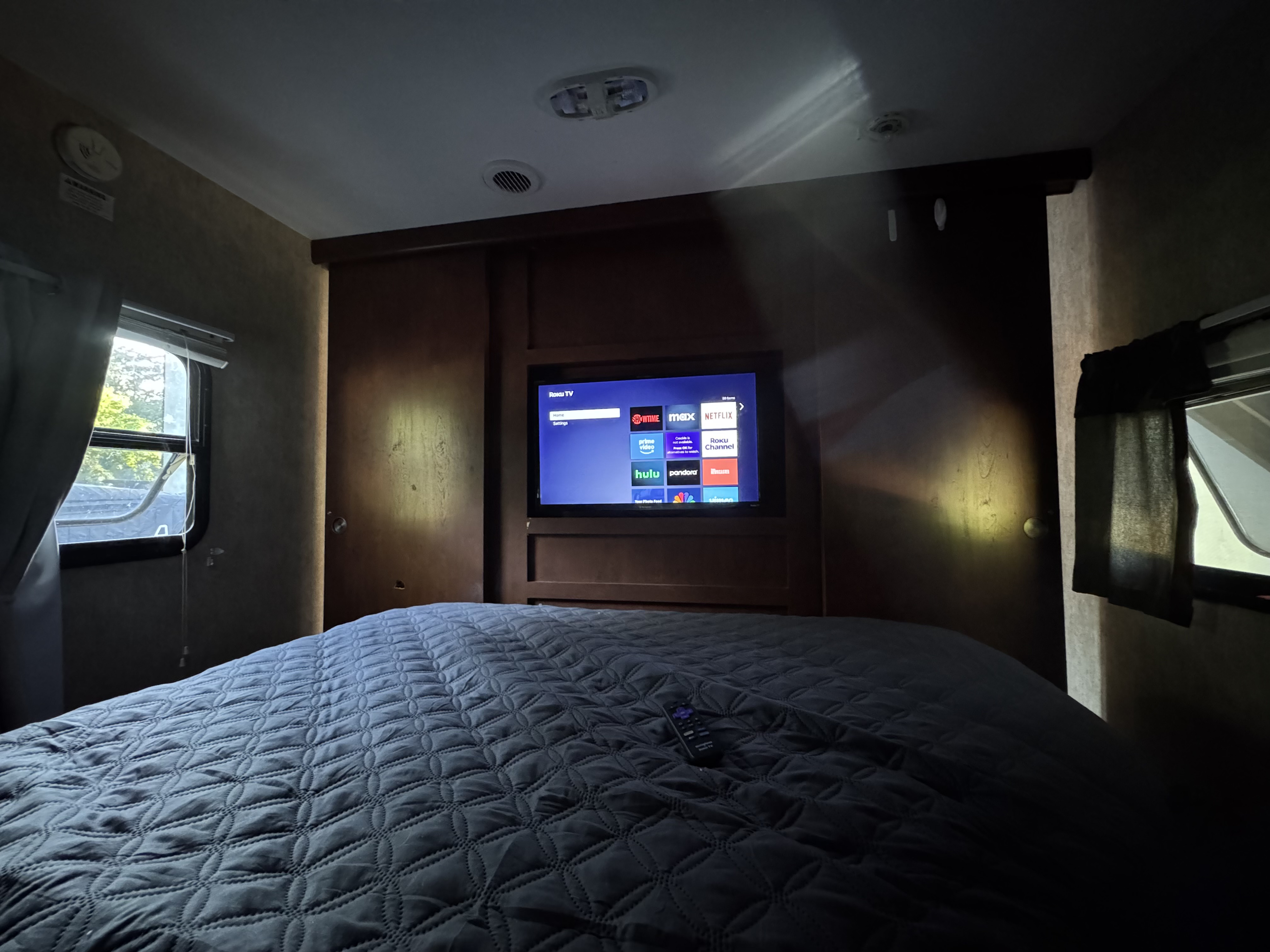 Cozy RV rental bedroom featuring a plush, quilted bed, a large Roku TV, and bright windows, ideal for unwinding.. Keystone RV Passport Grand Touring 2016