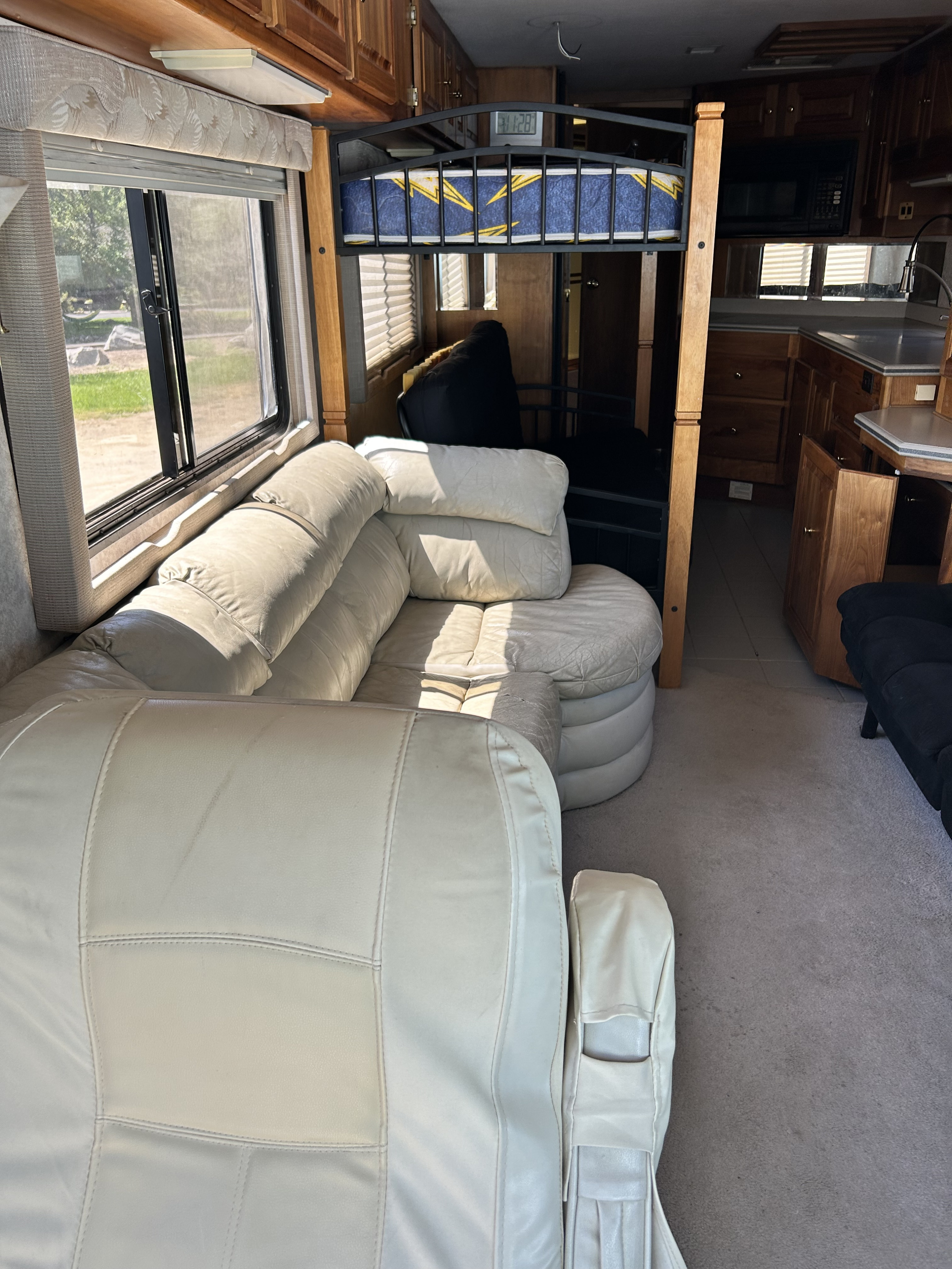 Interior of an RV rental showing cream sofas, a bunk bed, kitchen, and a large window with outdoor views.. Monaco Dynasty 1997