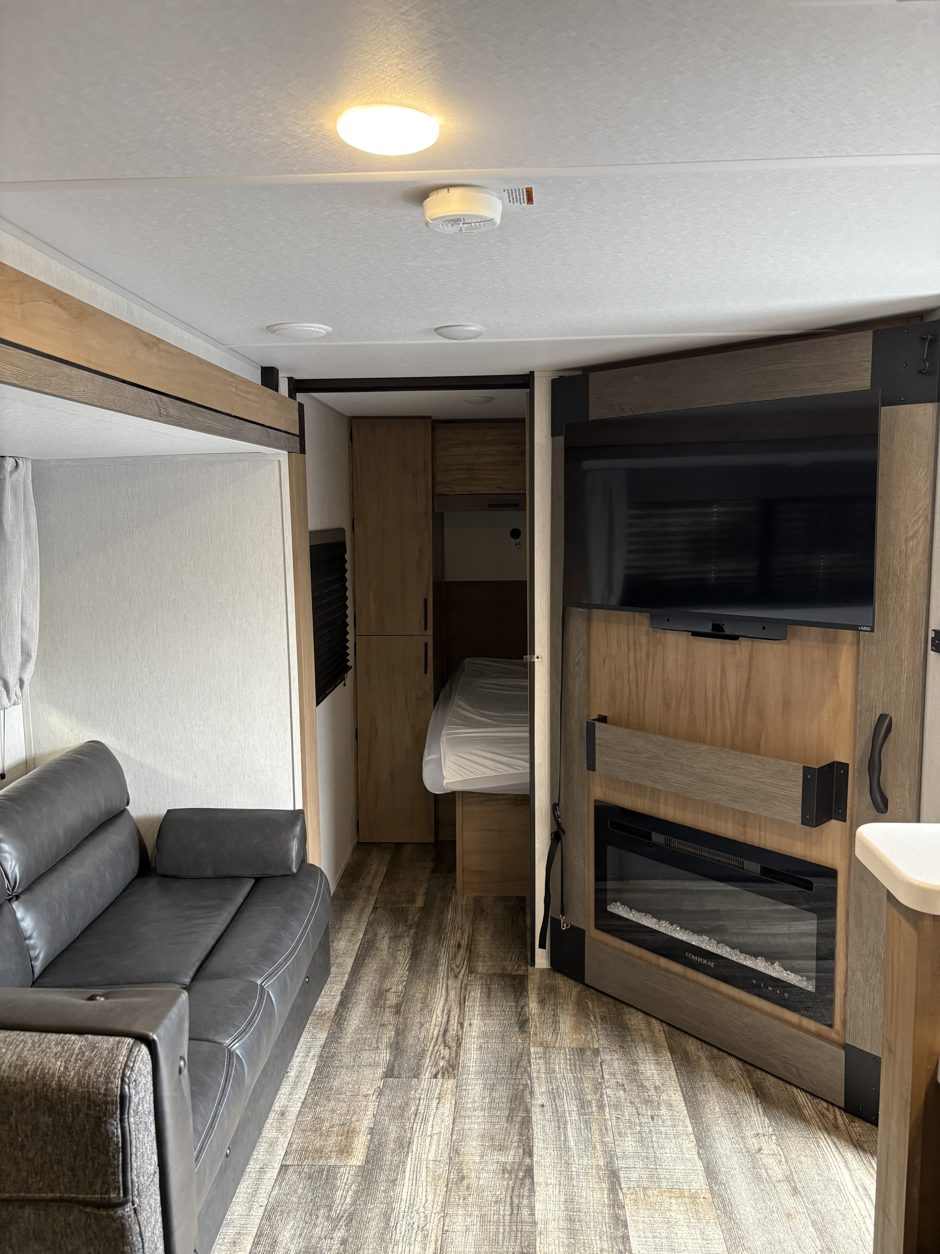 Modern RV rental interior with a comfy sofa, TV, electric fireplace, and a cozy bed nook, perfect for travel.. Forest River Campsite Reserve 2024