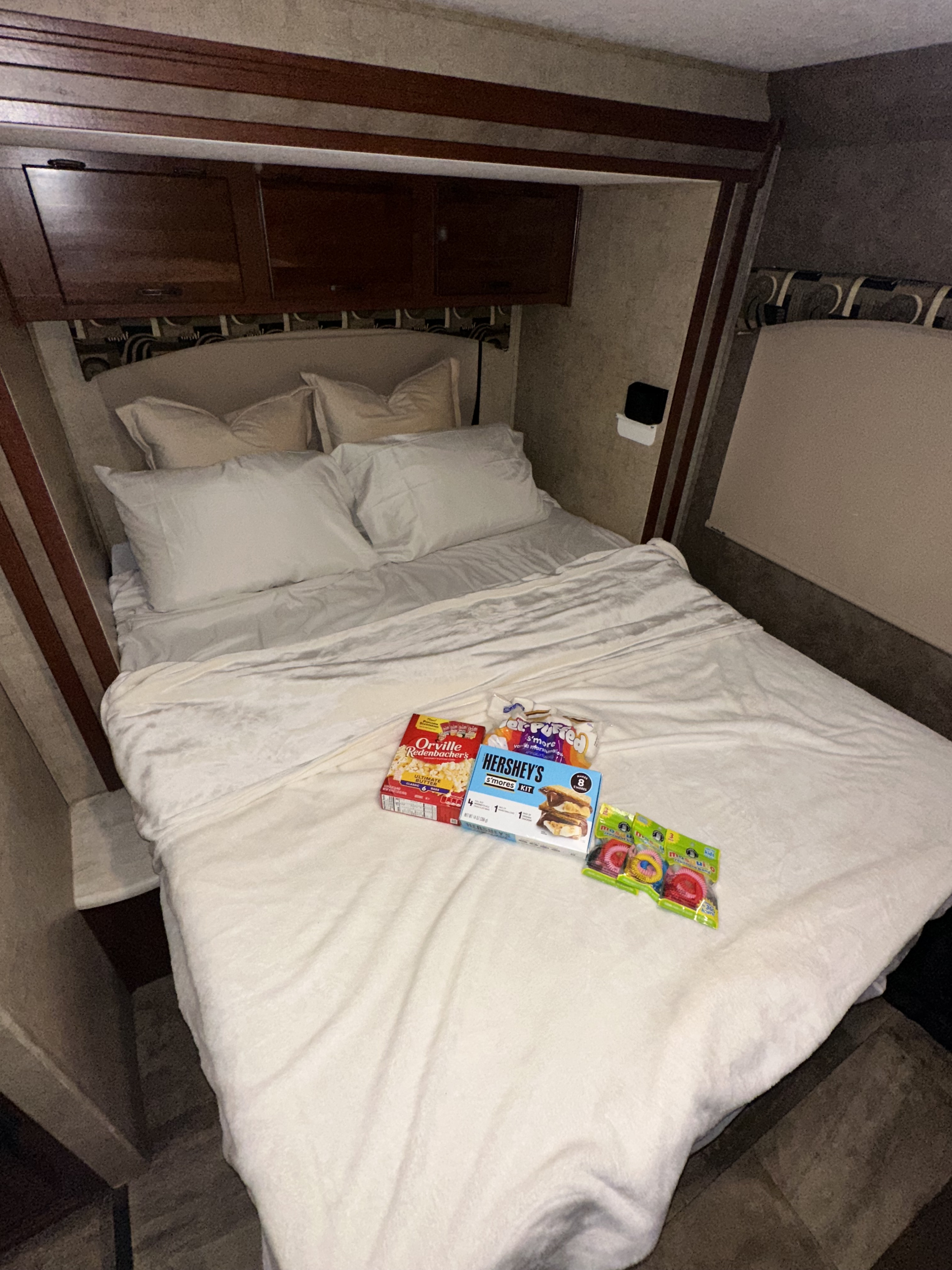 Cozy RV rental bed with white bedding, popcorn, Hershey's s'mores kit, marshmallows, and colorful hair ties.. Forest River Sunseeker 2016