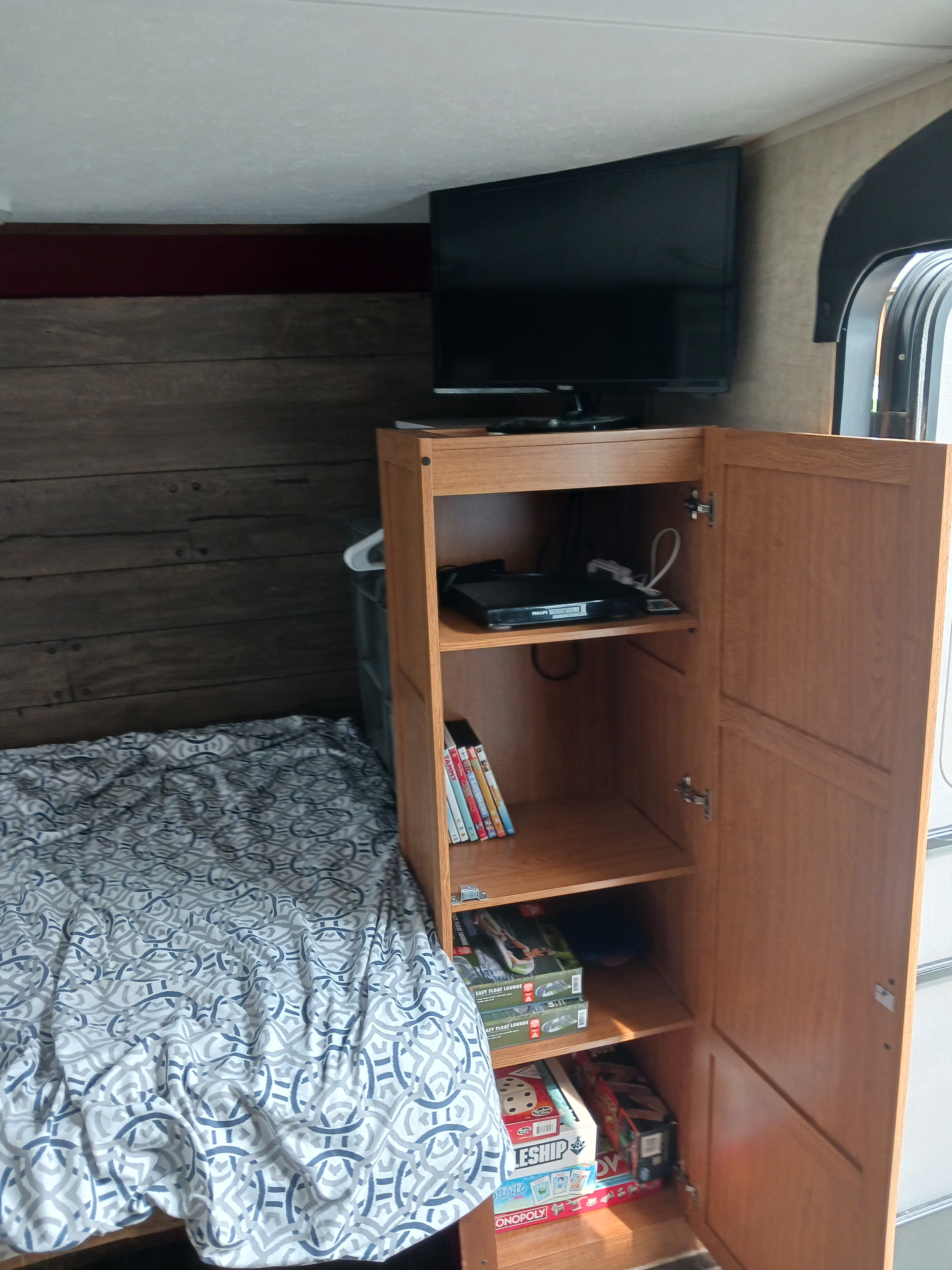 RV rental interior: cozy bedroom with TV, a media cabinet holding DVDs & board games, next to a patterned bed.. Keystone RV Hideout LHS 2015