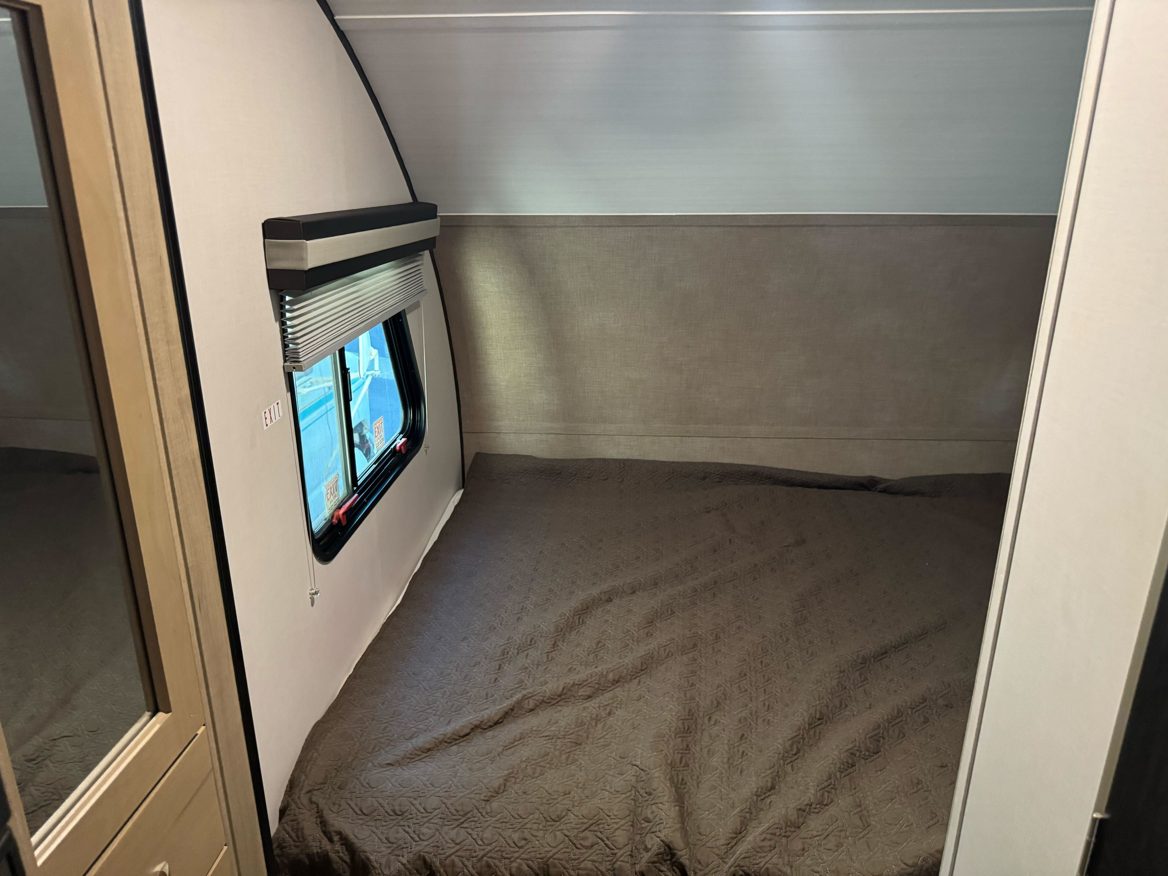 Cozy RV rental bedroom featuring a patterned bed, window with shade, and emergency exit.. Forest River RPod 189 2019