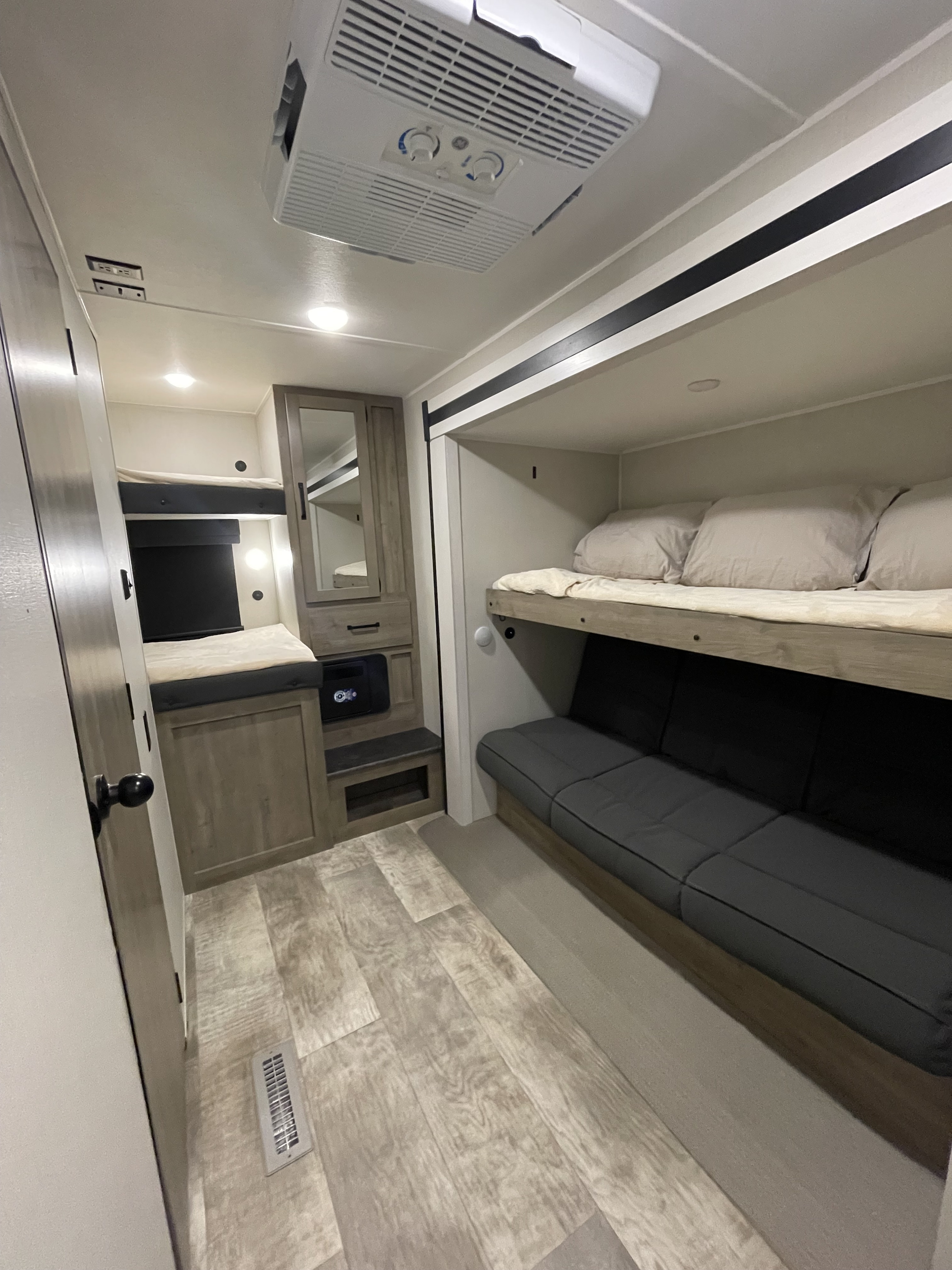 A modern rv rental interior showcasing comfortable bunk beds, a lower sofa, and a built-in AC unit, with wood-look flooring.. Forest River Palomino Puma 2024
