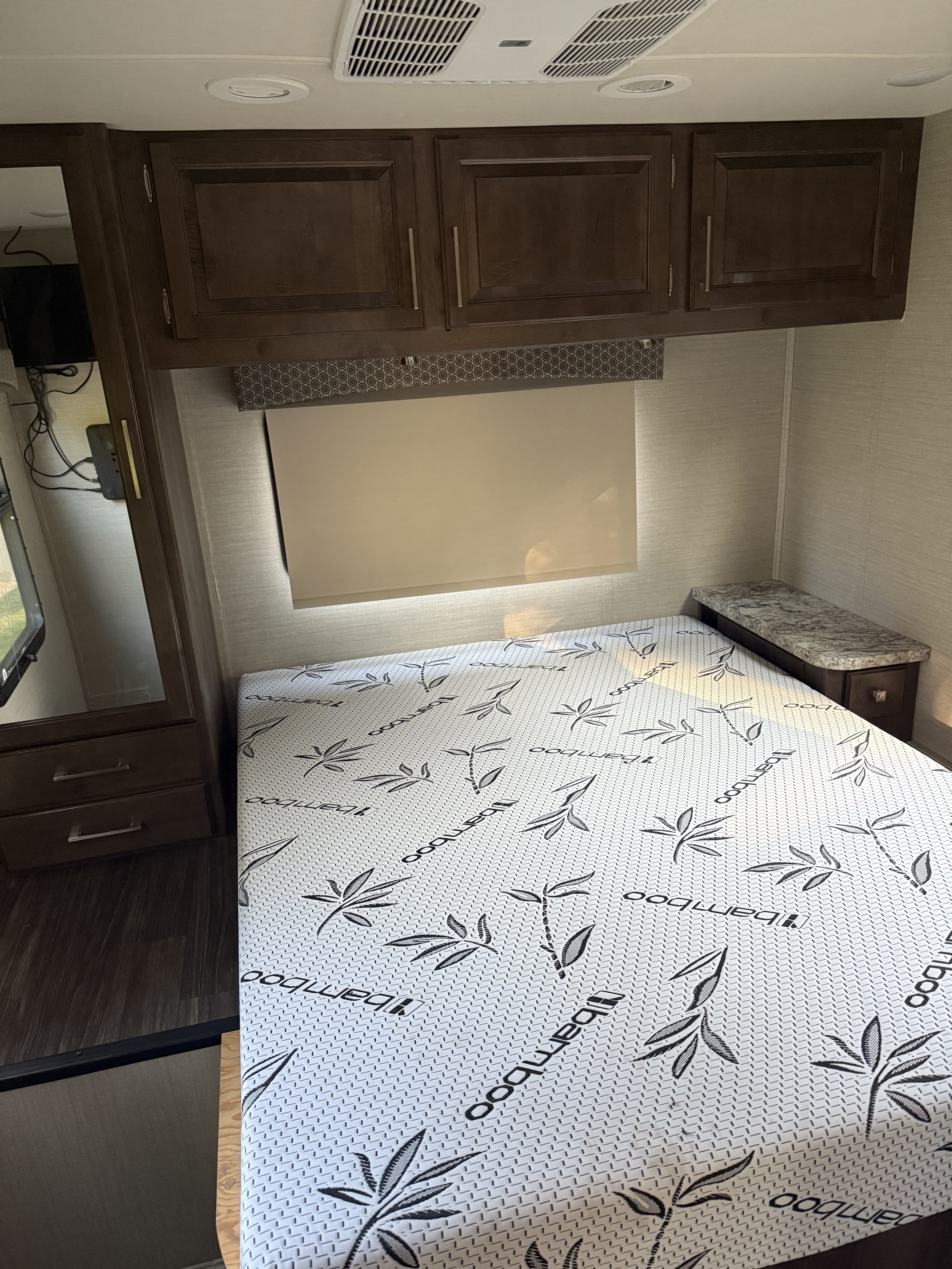 Cozy RV rental bedroom featuring a bamboo mattress, wooden cabinets, nightstand, and wardrobe area, perfect for travel.. Jayco Greyhawk 2018