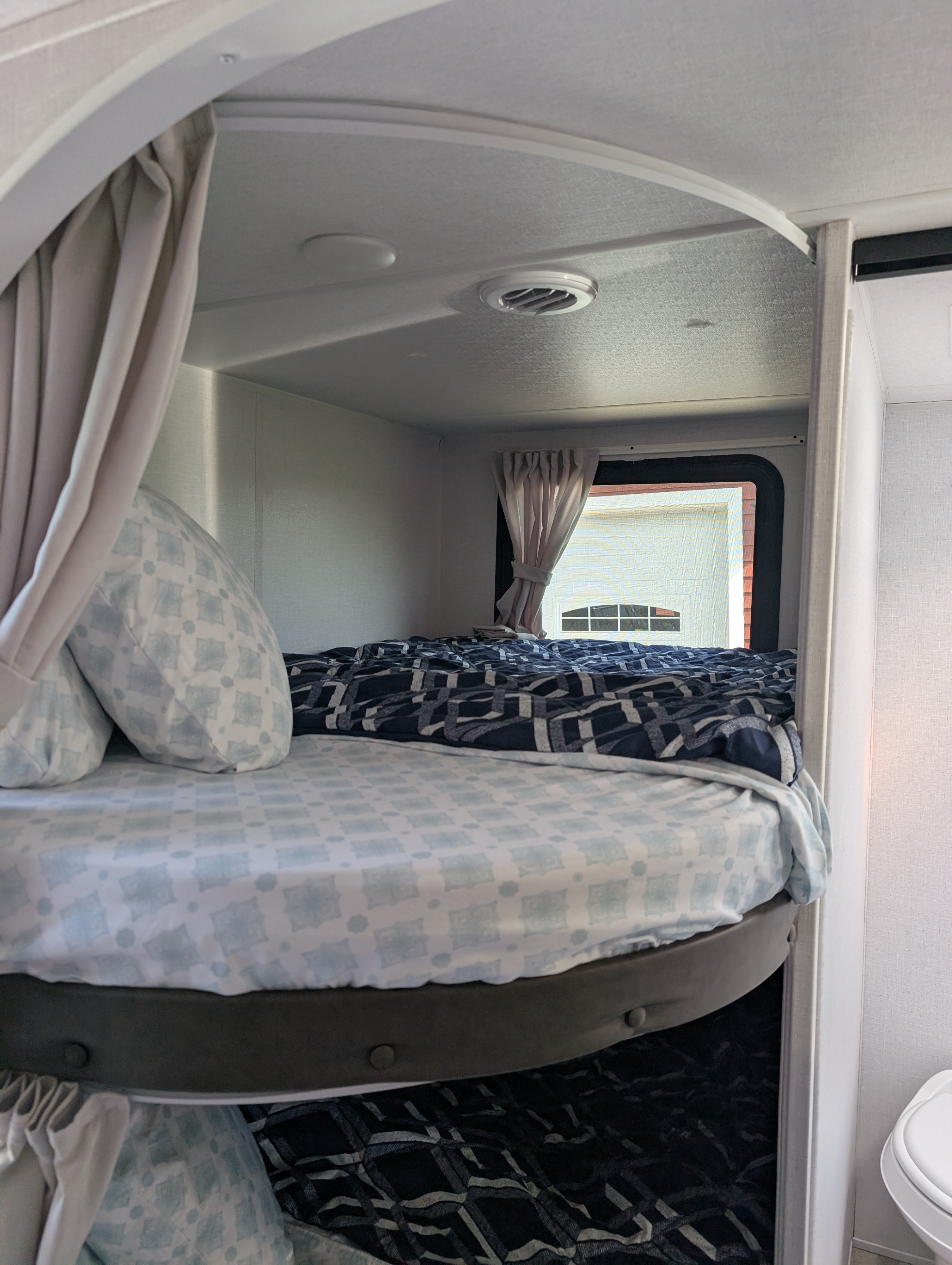 Cozy bunk beds in an RV rental, featuring light blue and dark patterned bedding, a window, and curtains.. Forest River Wildwood X-Lite 2025