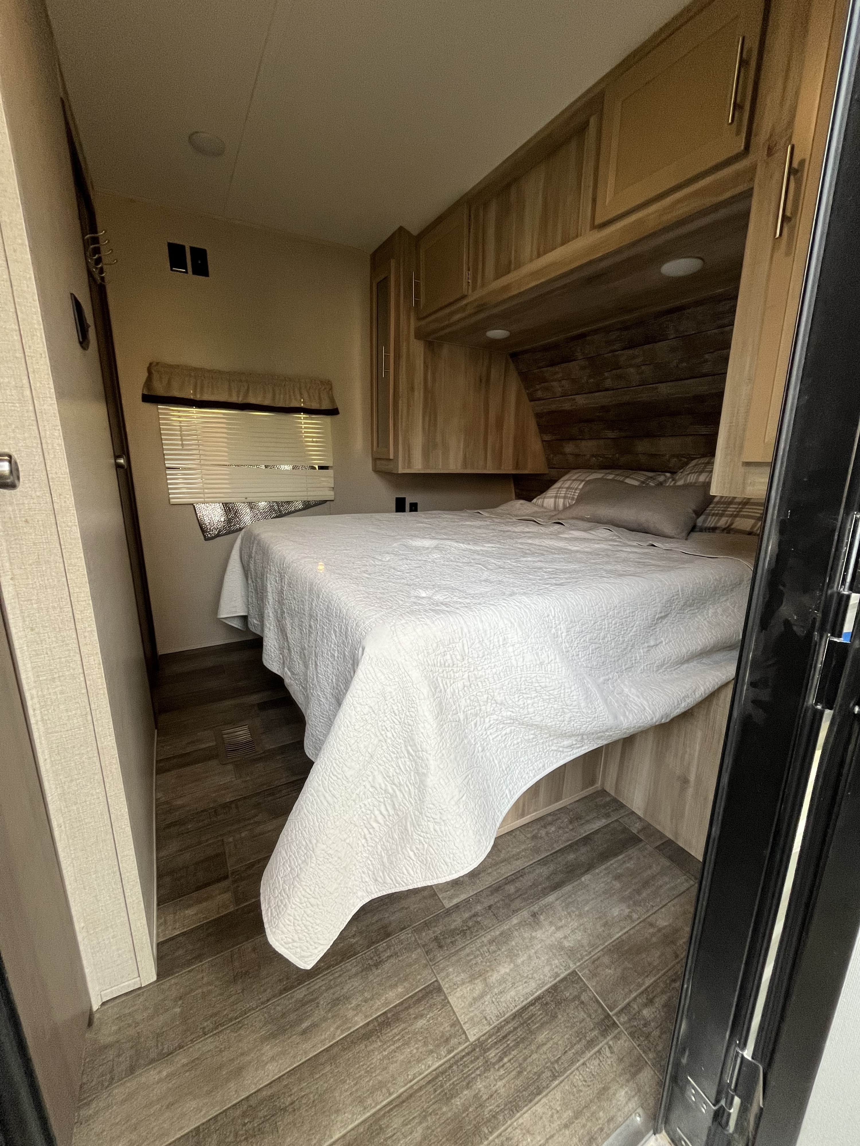 Cozy rv rental bedroom with a comfortable bed, wood-look flooring, and clever built-in storage for travel.. Forest River Coachmen Catalina Legacy 2021