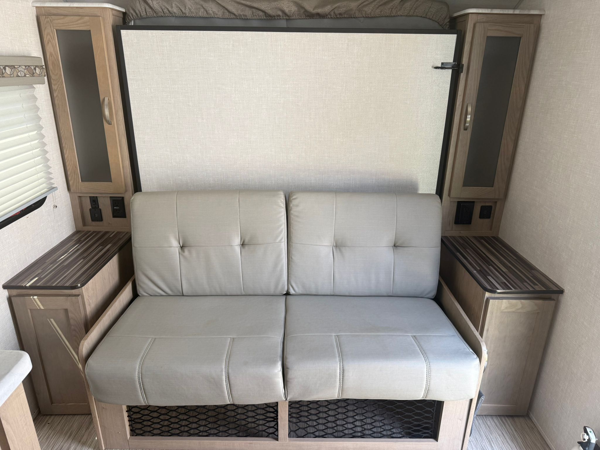 RV rental interior featuring a light sofa, fold-down bed, and wooden cabinets for versatile living.. R-Pod R-Pod Trailer 2020