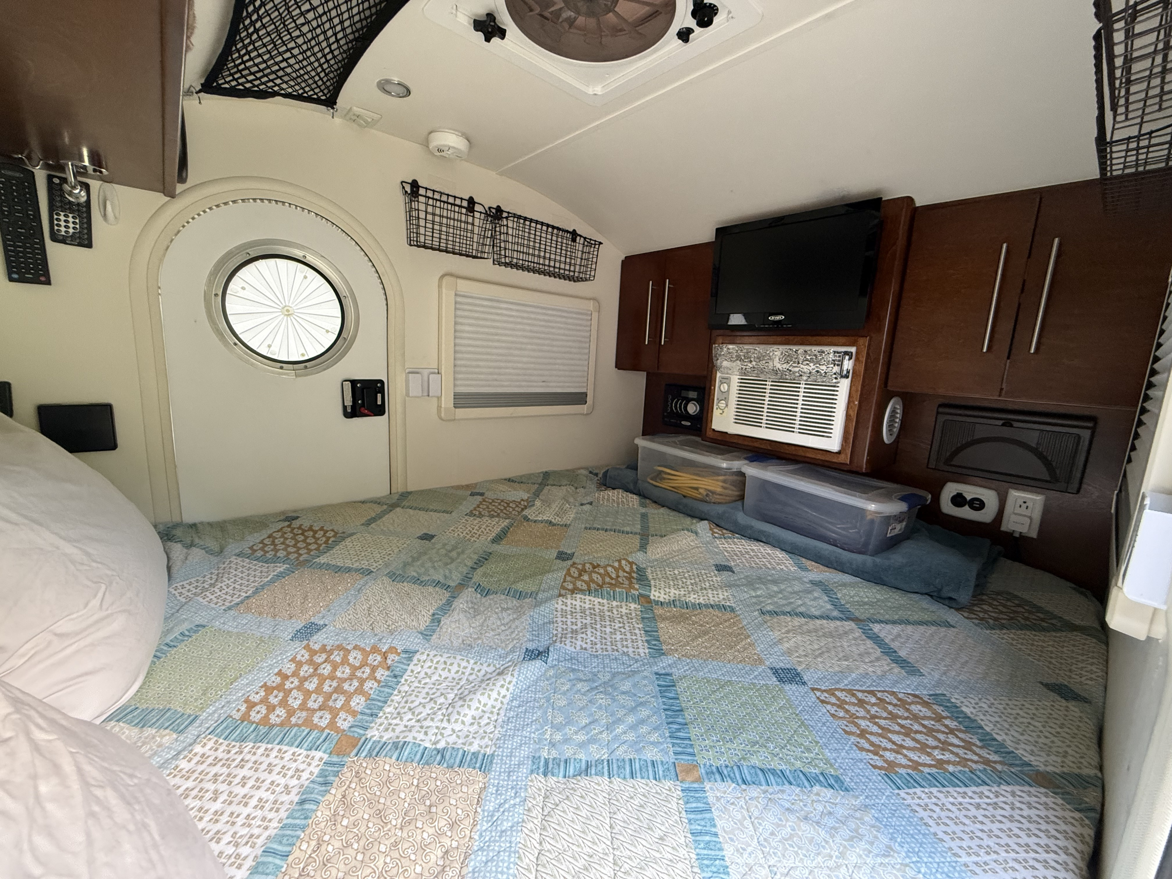 Cozy RV rental interior: a bed with patterned quilt, TV, AC, door, and built-in storage solutions.. Little Guy T@G 2016