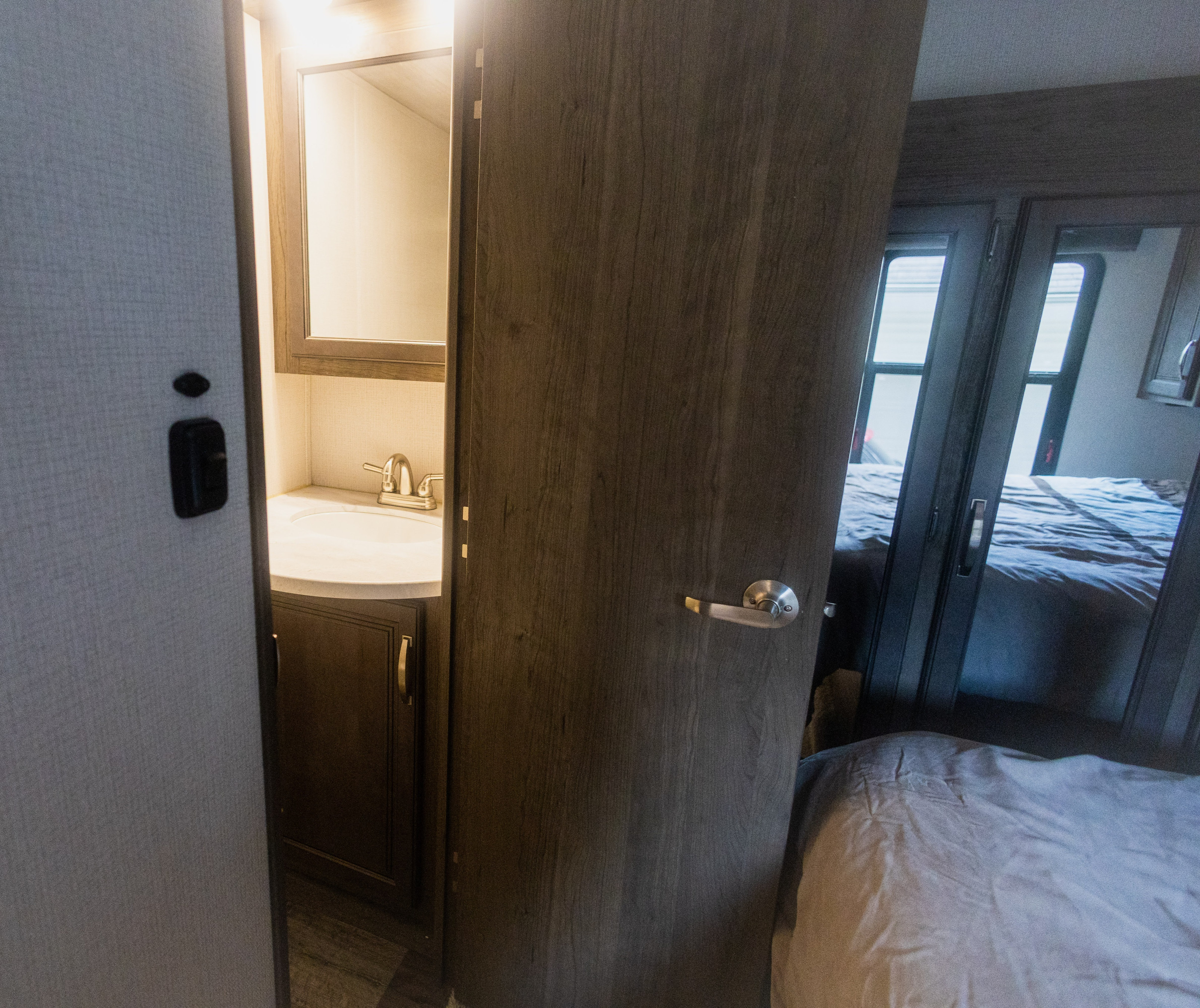 RV rental interior: A compact bathroom vanity with sink and lighted mirror, next to a bedroom with sliding mirrored closet doors.. Keystone RV Cougar 2022