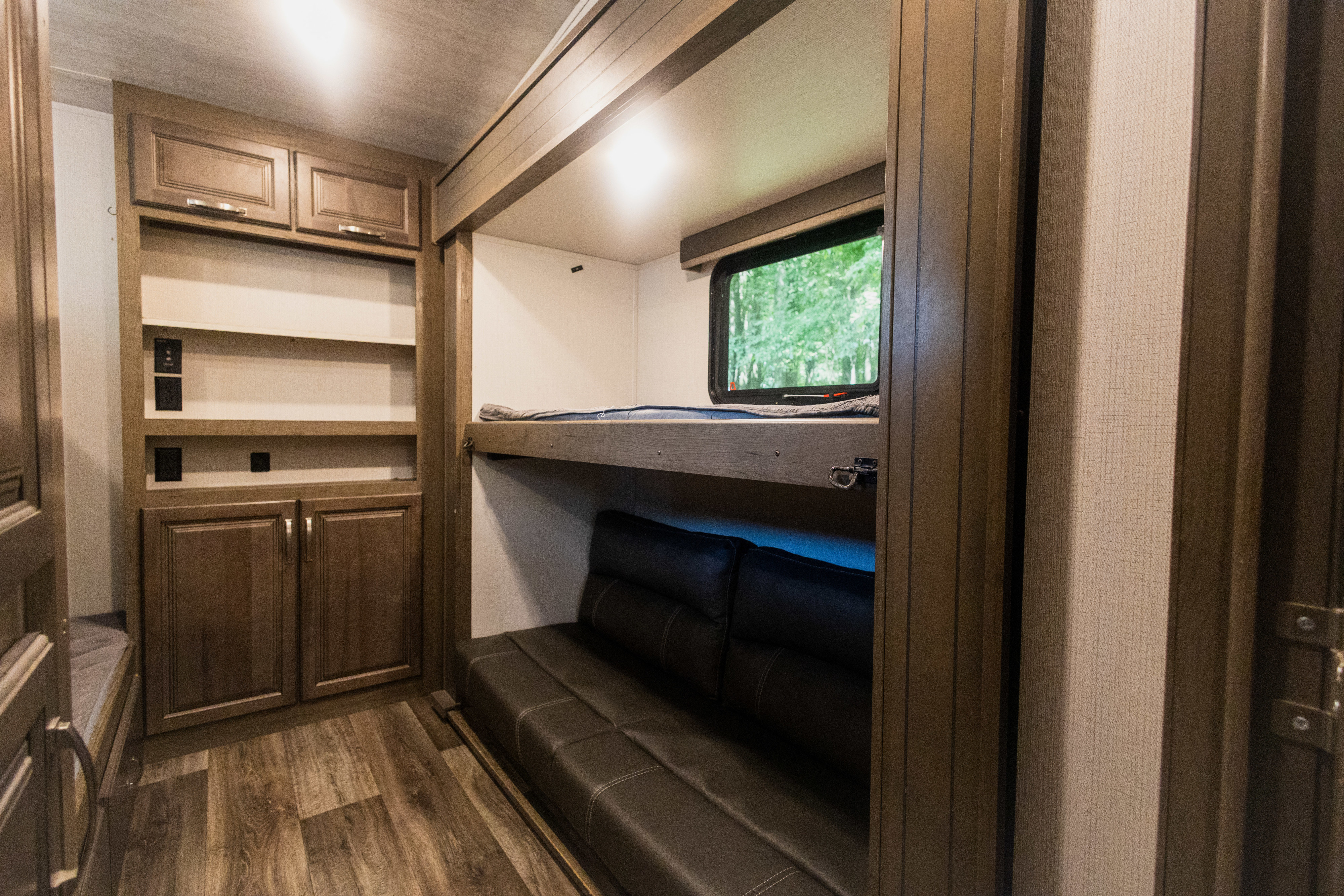 This RV rental interior features a bunk bed setup, convertible sofa, and built-in storage cabinetry on wood floors.. Keystone RV Cougar 2022