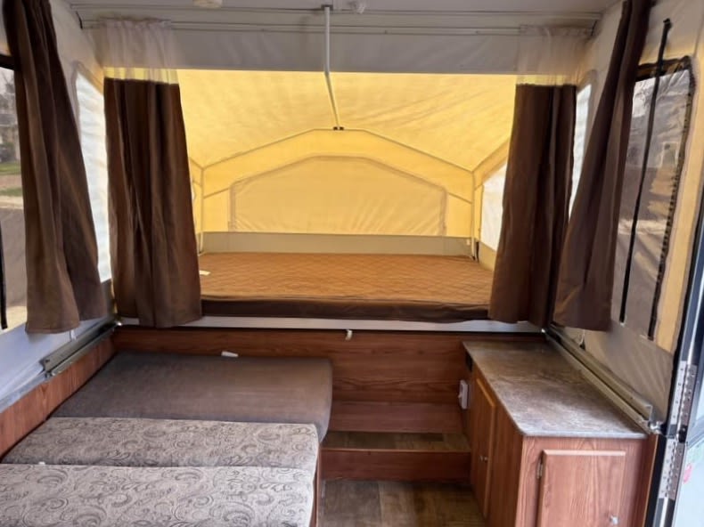 Inside a pop-up RV rental: a bed with brown mattress, patterned bench seating, and wood cabinetry on the right.. Rock wood 1940 LTD 2016