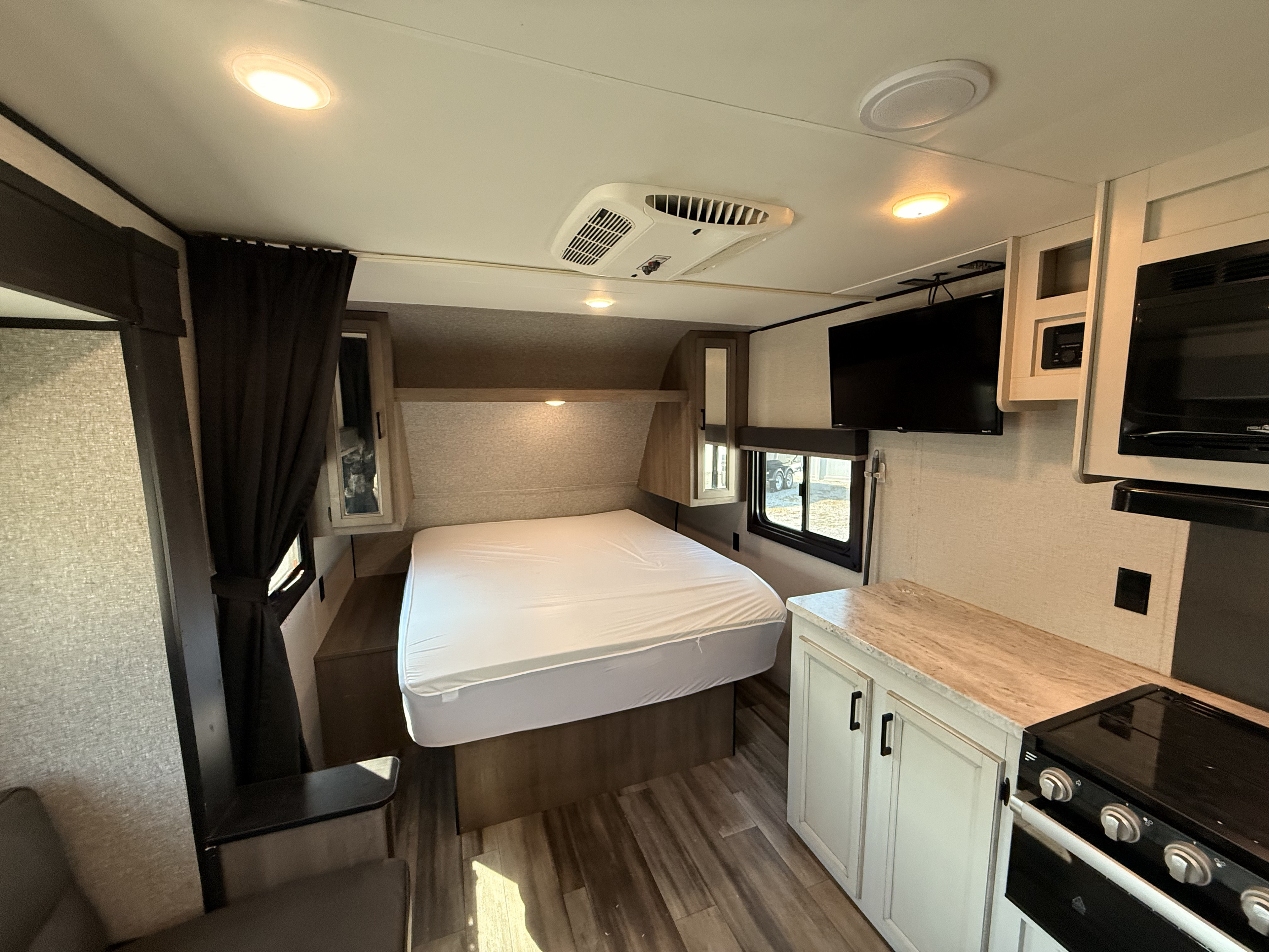 Modern RV rental interior: bedroom with a bed, kitchen counter with stove, and living area with TV.. Highland Ridge RV Open Range 2022