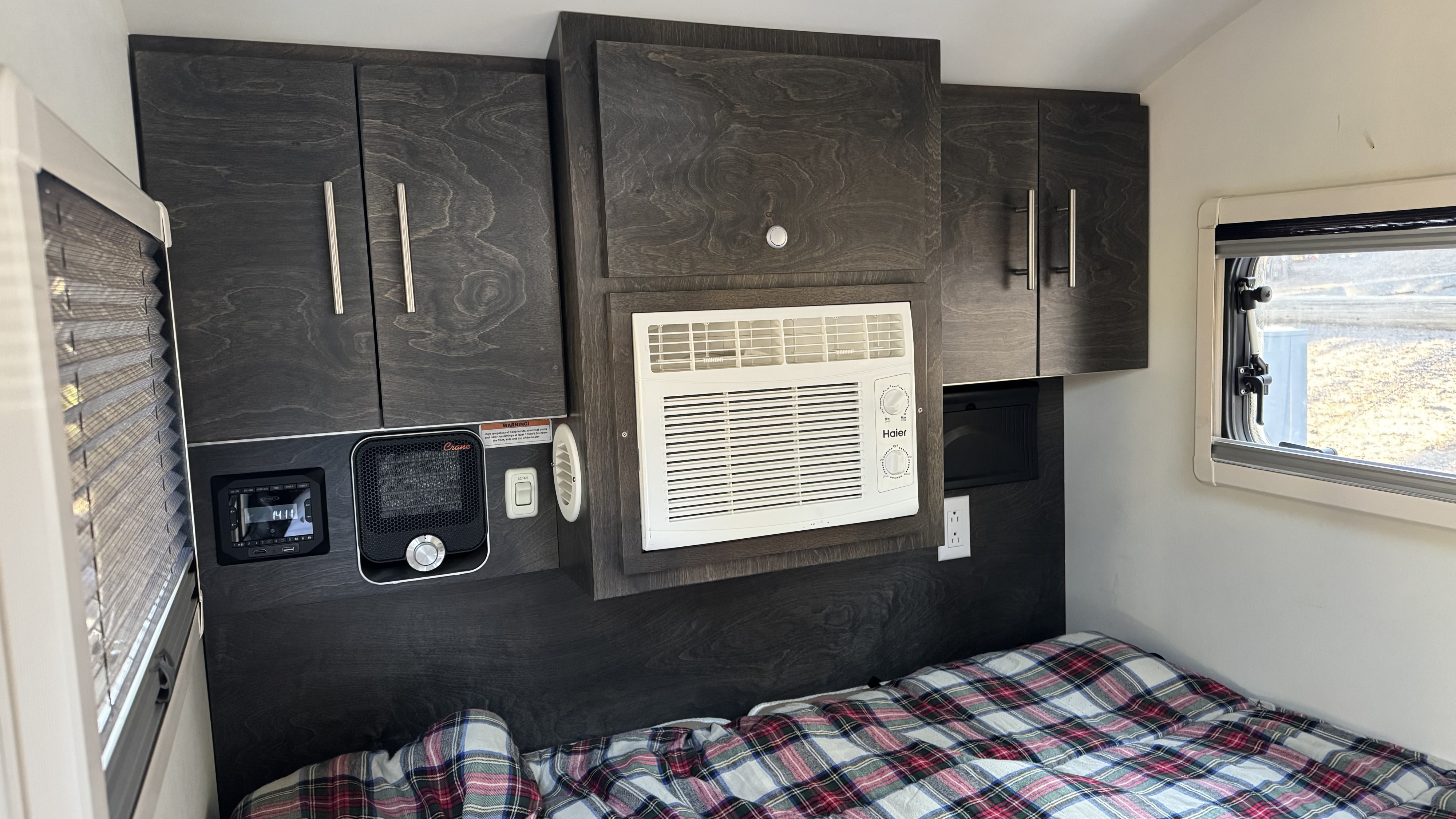 Cozy RV rental interior with bed, dark cabinetry, AC, heater, and control panel for comfort.. nuCamp T@G 2021