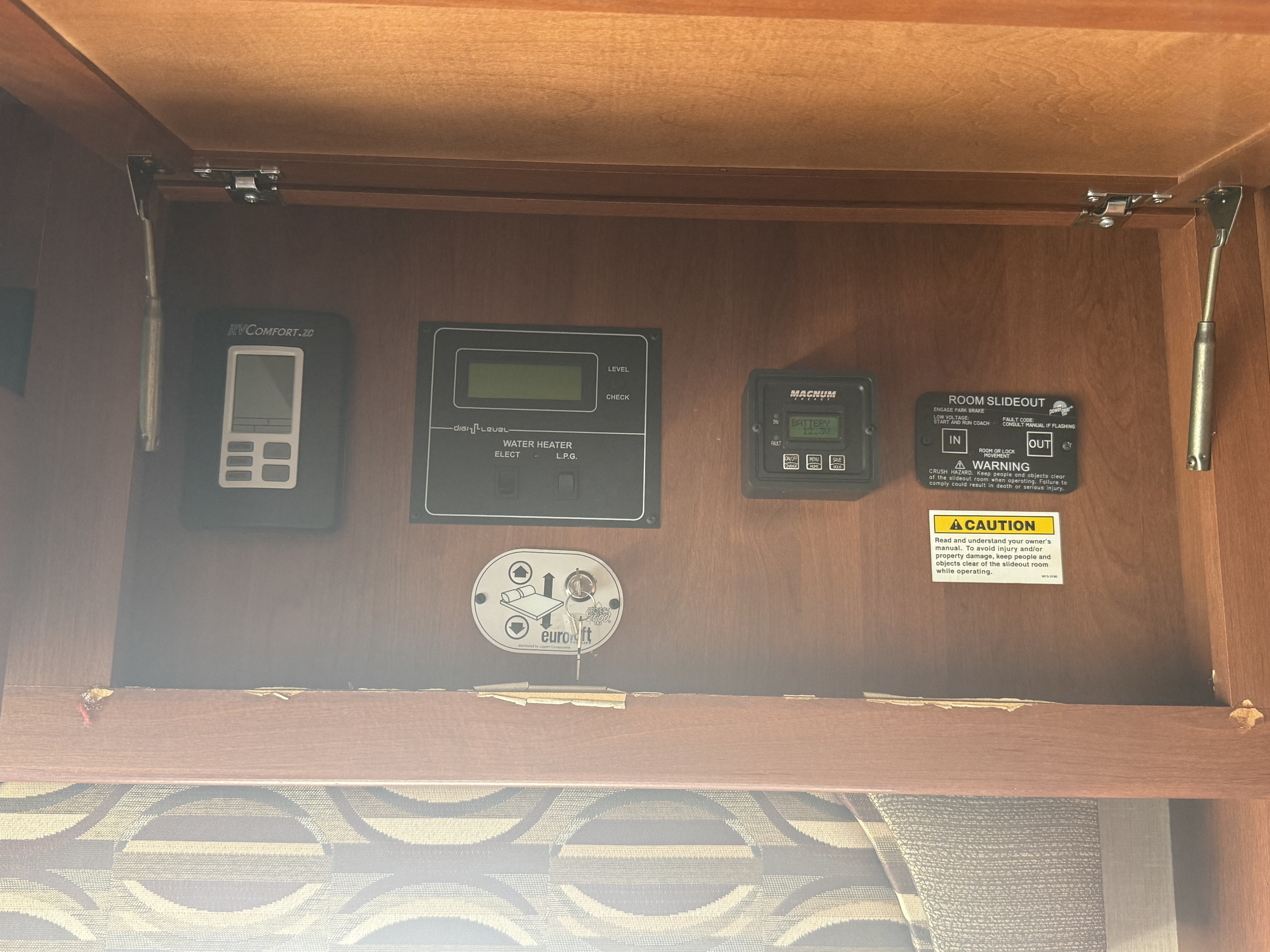RV rental control panel in a wooden cabinet. Features AC, water/LPG levels, battery monitor, room slideout, and EuroLift bed controls.. Fleetwood Bounder 2016