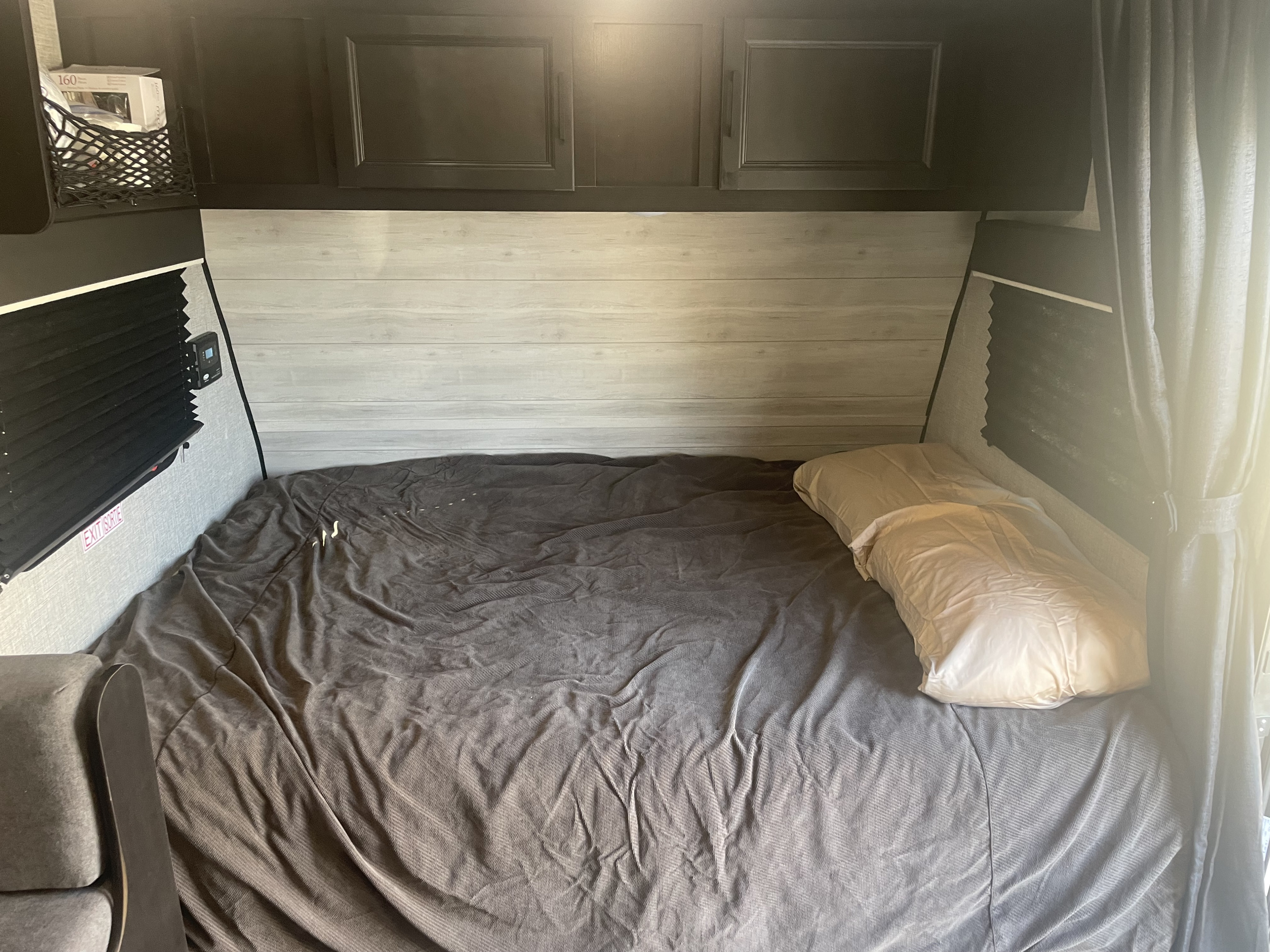 Cozy RV rental sleeping area: bed with textured bedding, wood-look headboard, overhead cabinets, and window blinds.. Jayco Jay Feather 2021
